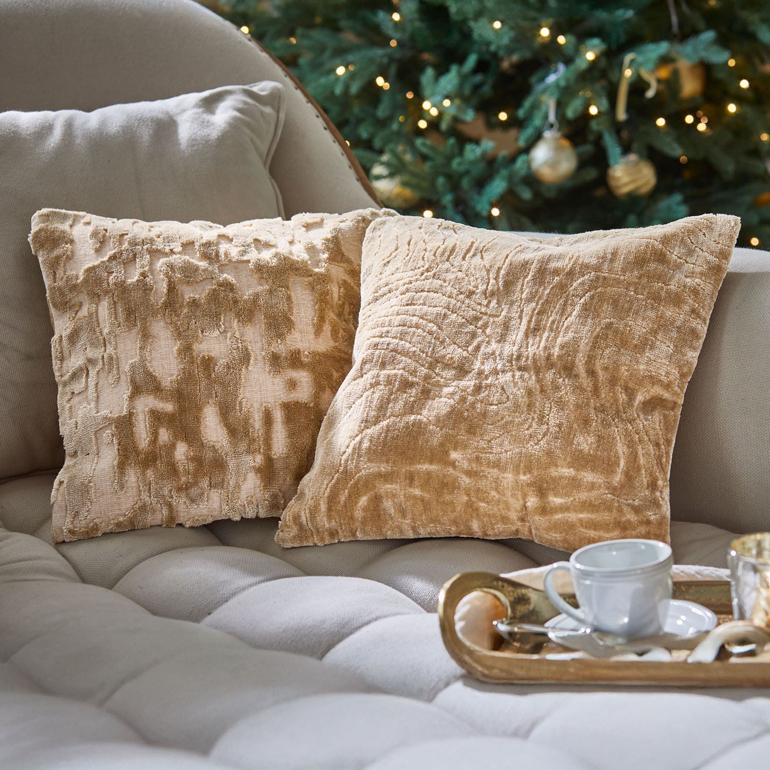 Zwei beige dekorative Kissen aus weichem Material auf hellem Sofa vor geschmücktem Weihnachtsbaum