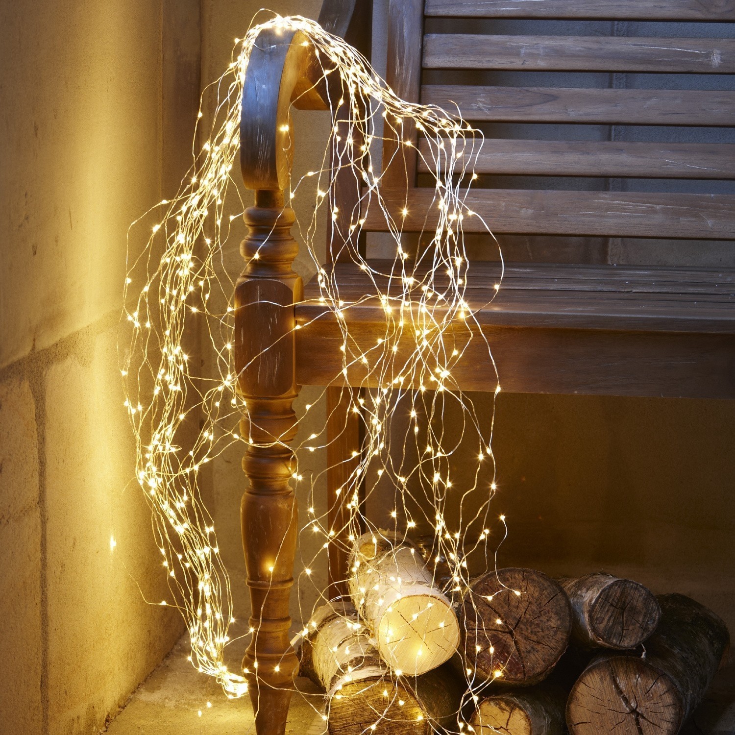 Lichterkette Voltage Feine warmweiße LED-Lichterkette auf dünnen Drähten um eine Holzbank und Holzscheite gewickelt