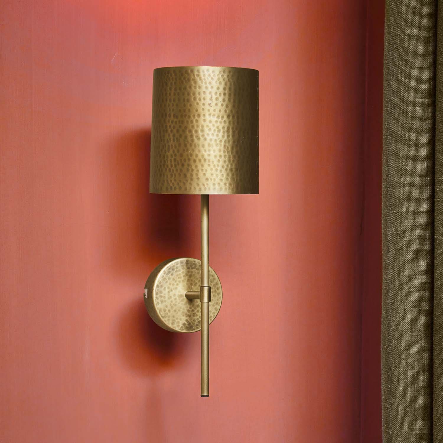 Wandlampe aus gehämmertem Messing mit zylindrischem Schirm an roter Wand, dekorative Beleuchtung