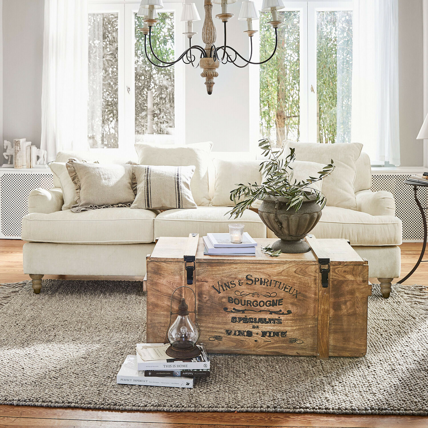 Holztruhe mit Vintage-Schriftzug als Couchtisch im hellen Wohnzimmer mit beigem Sofa und Dekoration