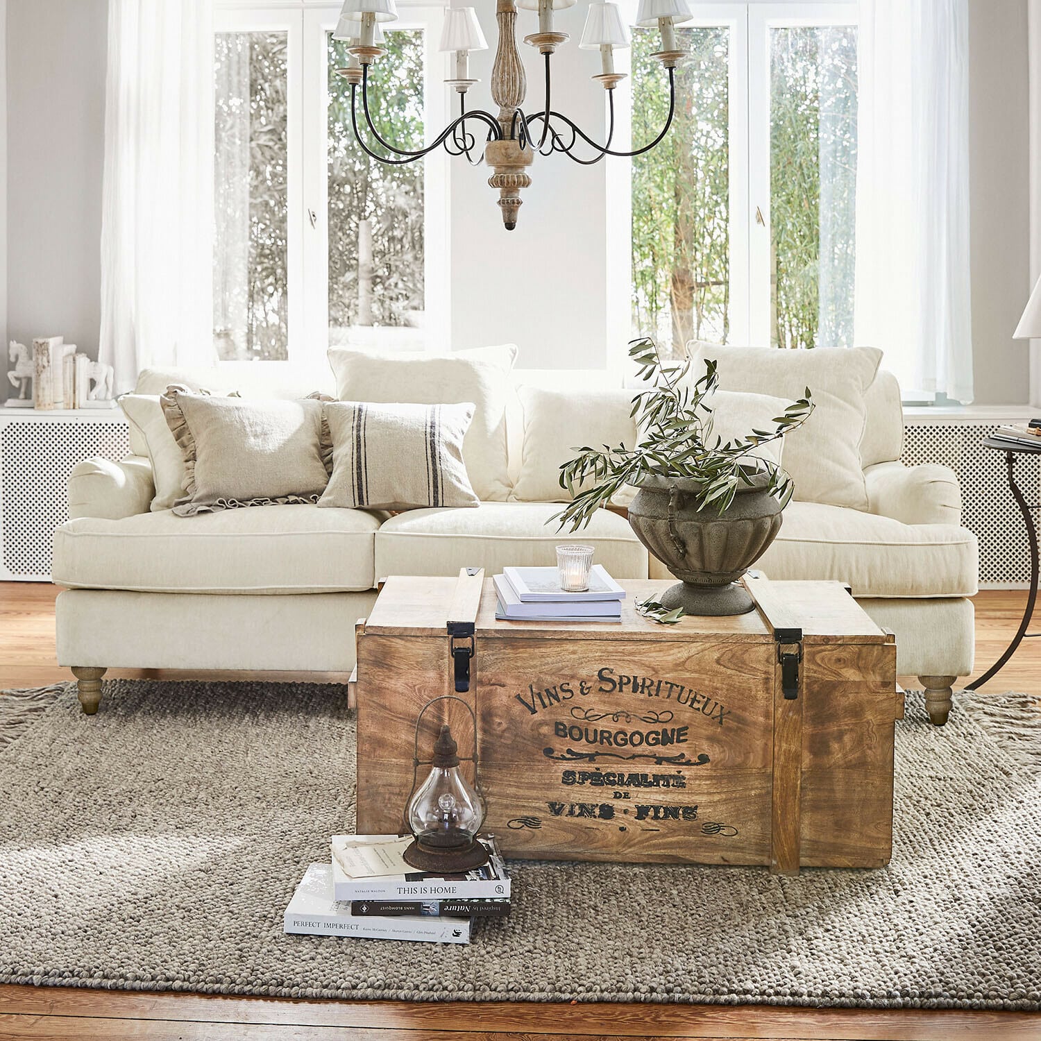 Sofa Isa Holztruhe mit Vintage-Schriftzug als Couchtisch im hellen Wohnzimmer mit beigem Sofa und Dekoration