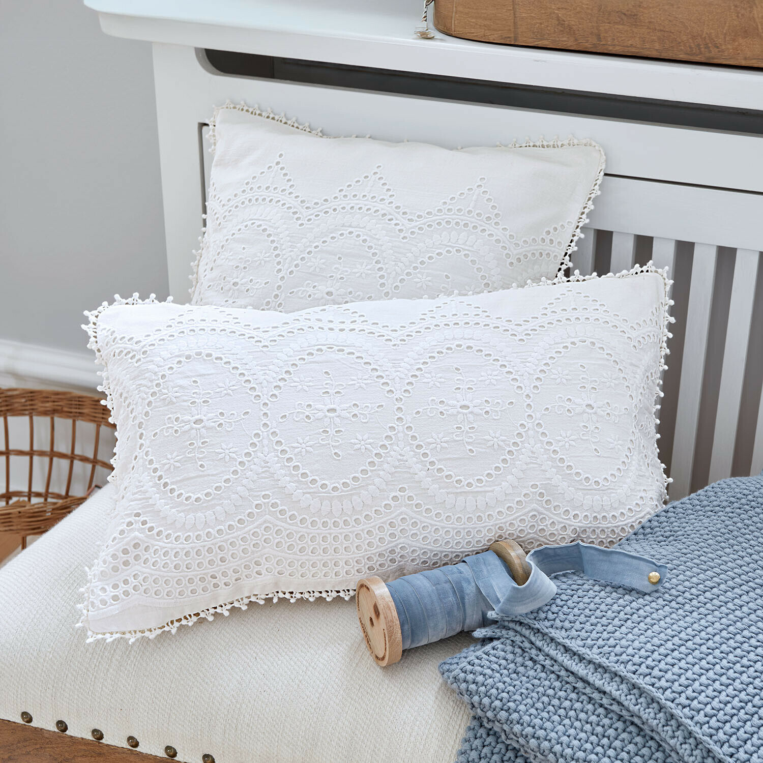 Weiße Baumwollkissen mit Stickerei und Lochmuster auf Sofa mit blauem Strickdecke