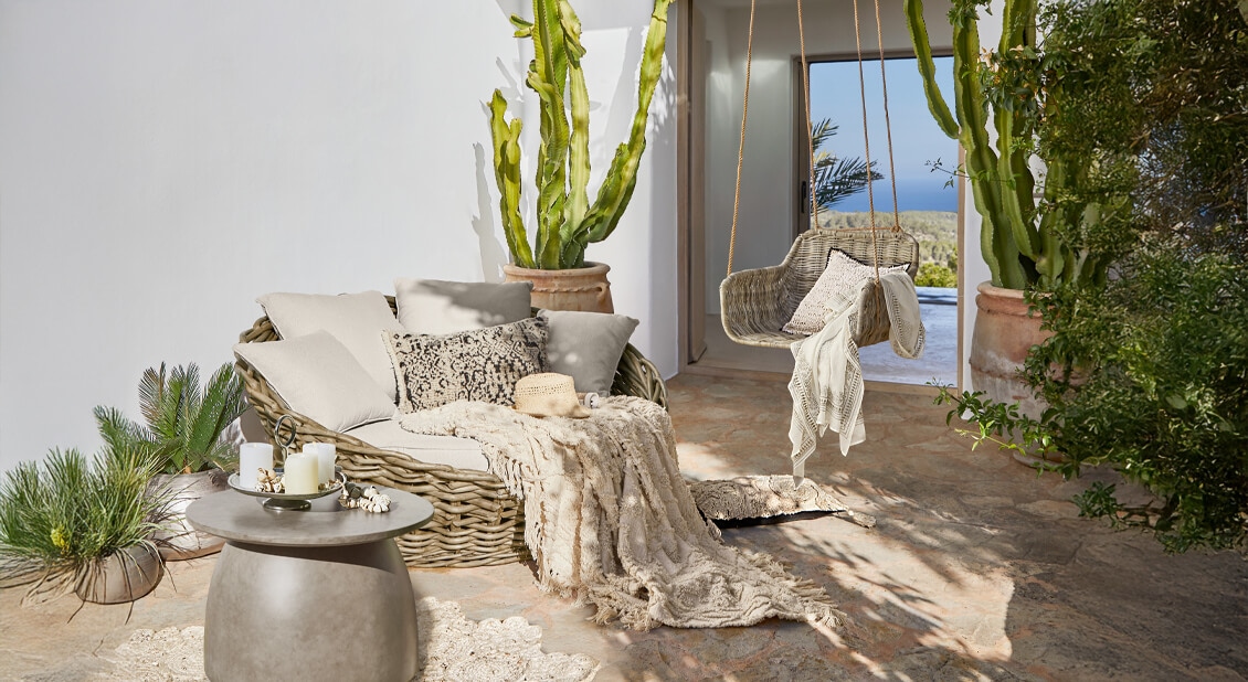 Gemütliches Rattan-Sitzmöbel-Set in Beige mit Kissen und Decke auf sonniger Terrasse mit Meerblick