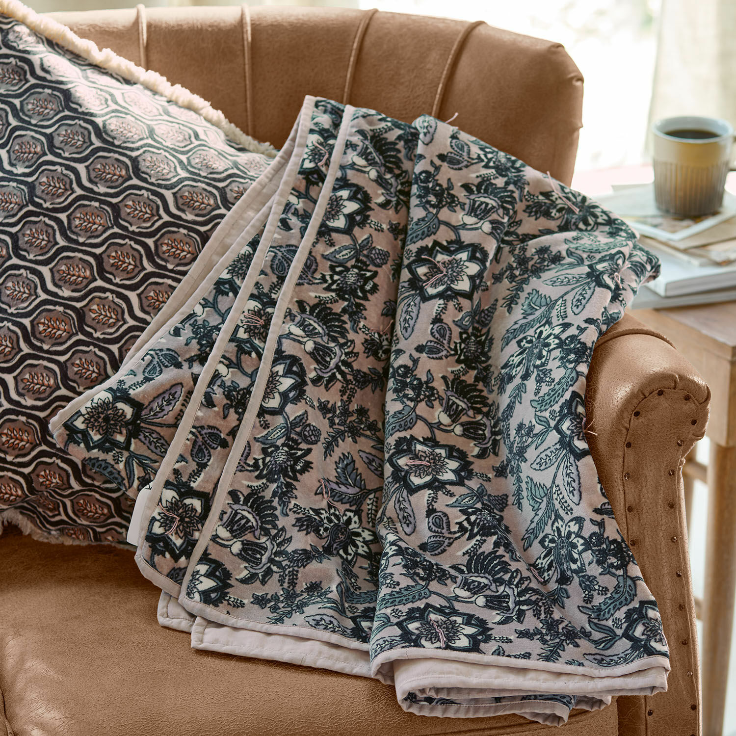 Plaid Elarion Weiche Decke mit grauem Blumenmuster auf beigem Sofa mit gemustertem Zierkissen