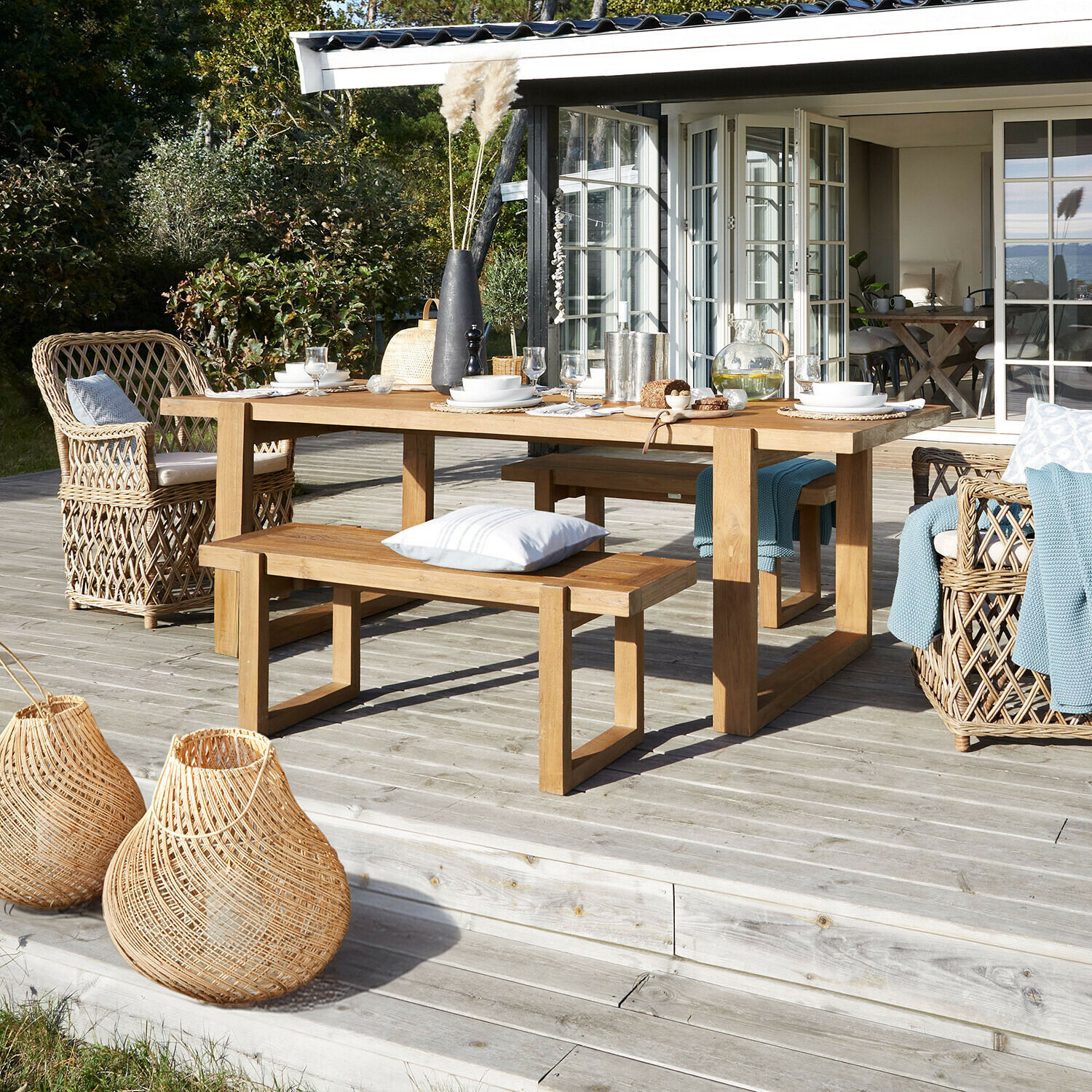 Bank Halinor Holz-Gartentisch mit Bänken und Rattansesseln auf Holzterrasse mit natürlichen Dekorationen