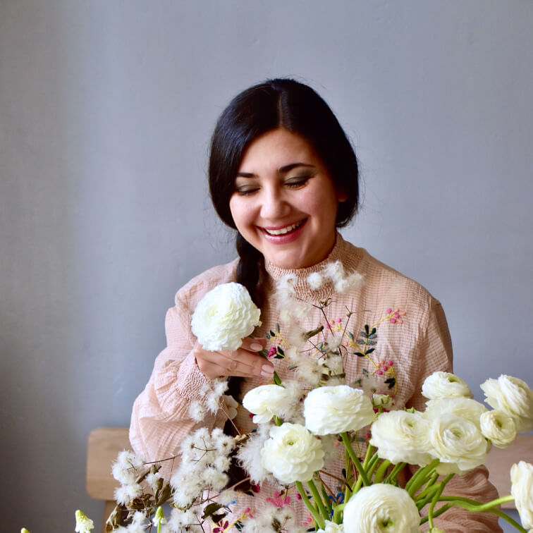Frau in rosa bestickter Bluse hält weiße Ranunkelblumen in hellem Raum