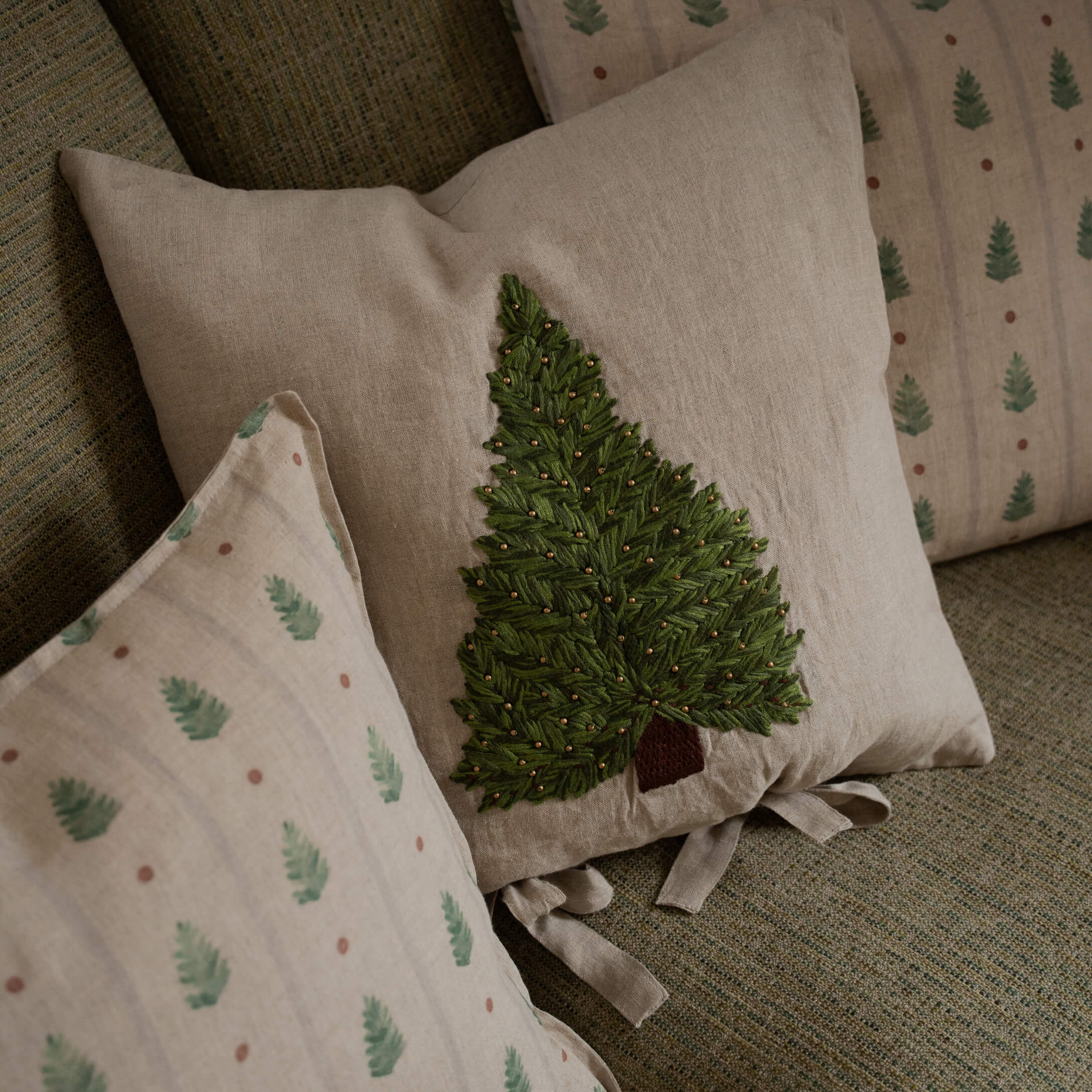 Beige Leinenkissen mit grün besticktem Baum und dekorativen Perlen auf Sofa