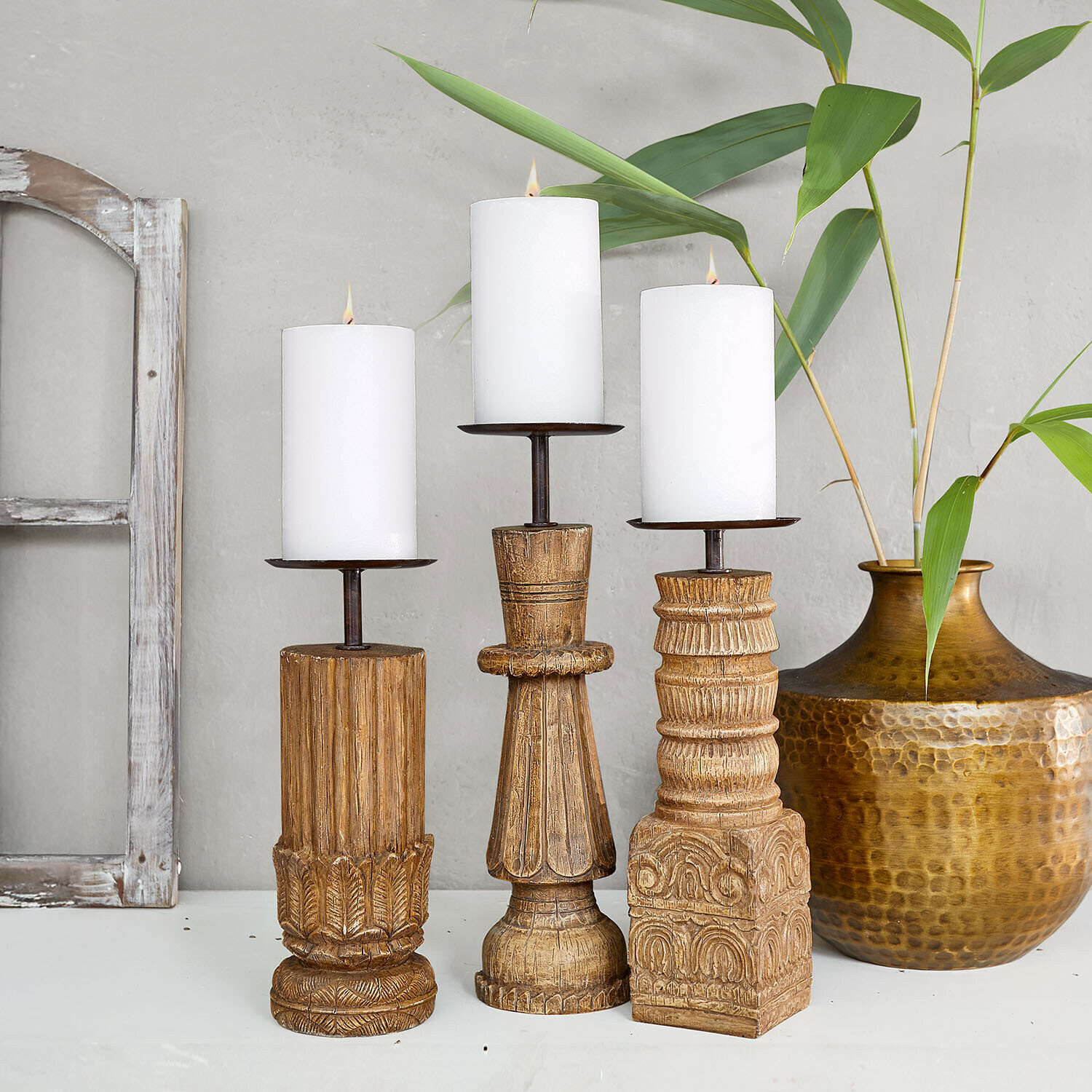 Drei geschnitzte Holzkerzenhalter mit weißen Kerzen, naturfarbene Oberfläche und dekorative Muster