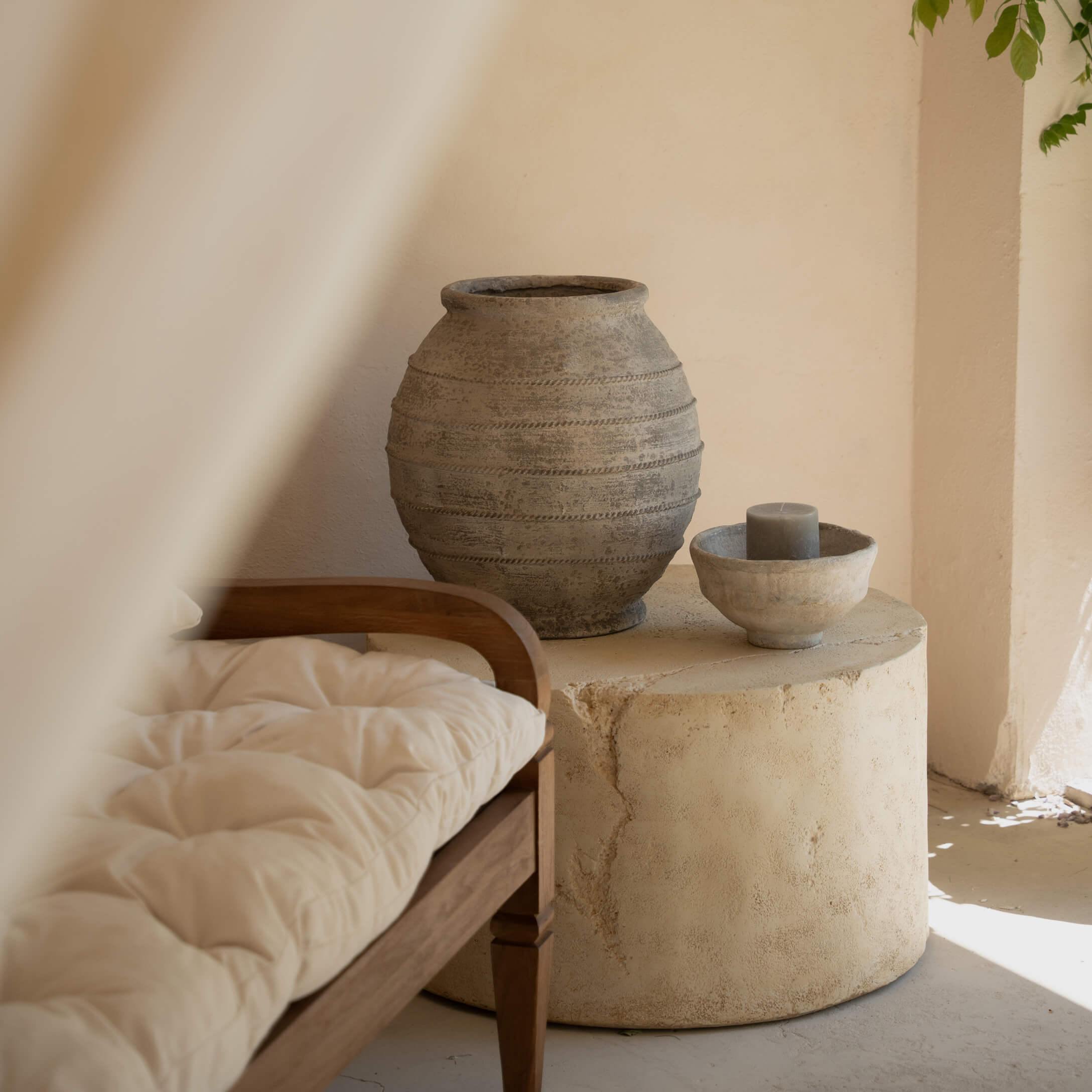 Runder Steintisch mit grauem Keramikvase und Kerze in hellem Raum mit Holzbank