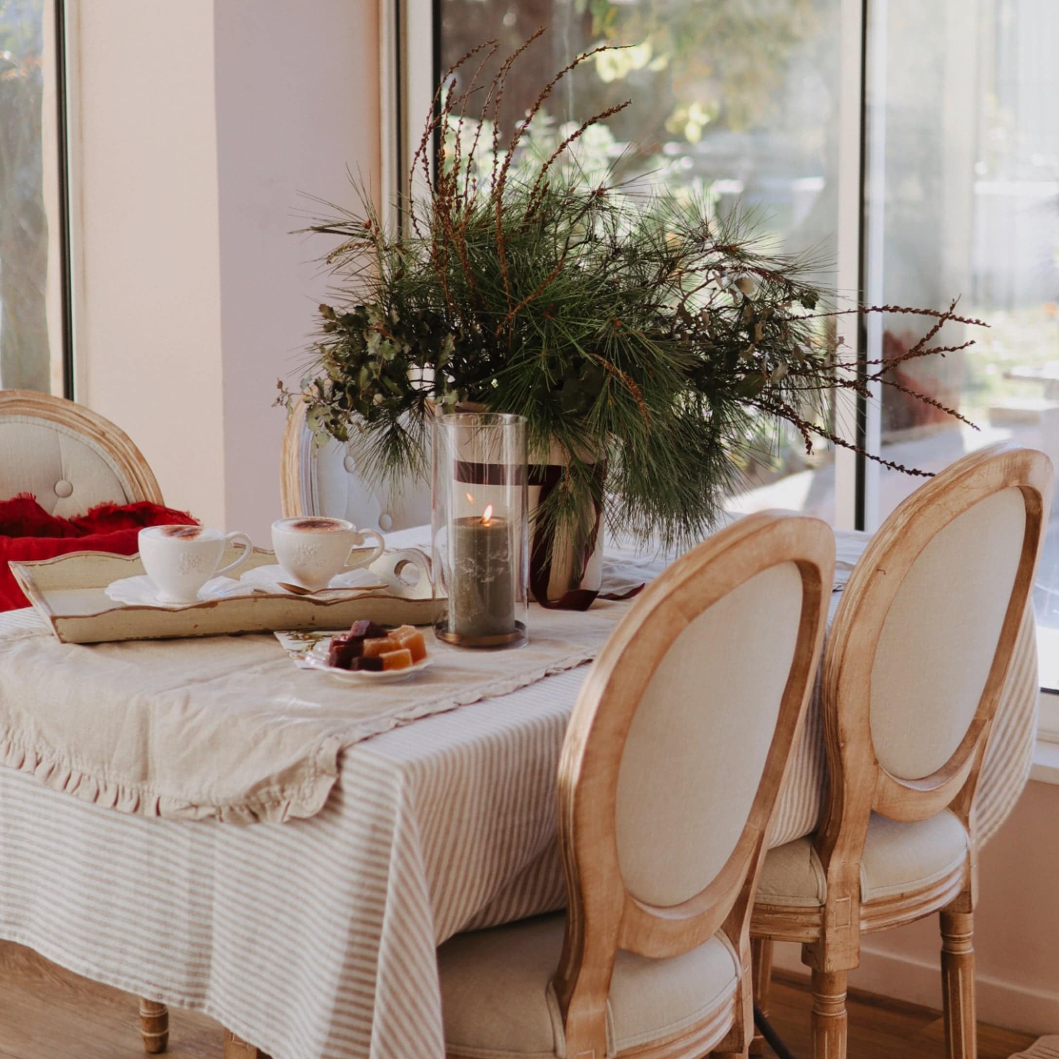 Gemütlicher Tisch mit beigem Tischläufer, Holzstühlen und weihnachtlicher Dekoration aus grünen Zweigen