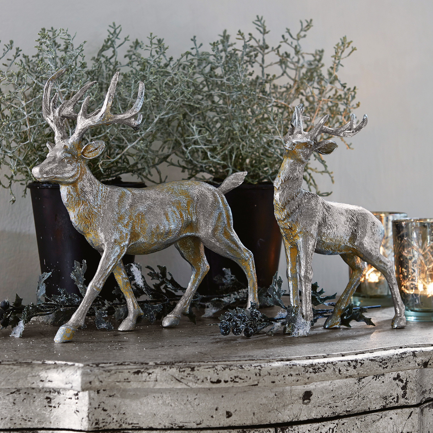 Hirsche 2er Set Rudy & Son Zwei silberne Hirsch-Dekorationen aus Kunststoff auf rustikalem Sideboard mit Pflanzen und Kerzen