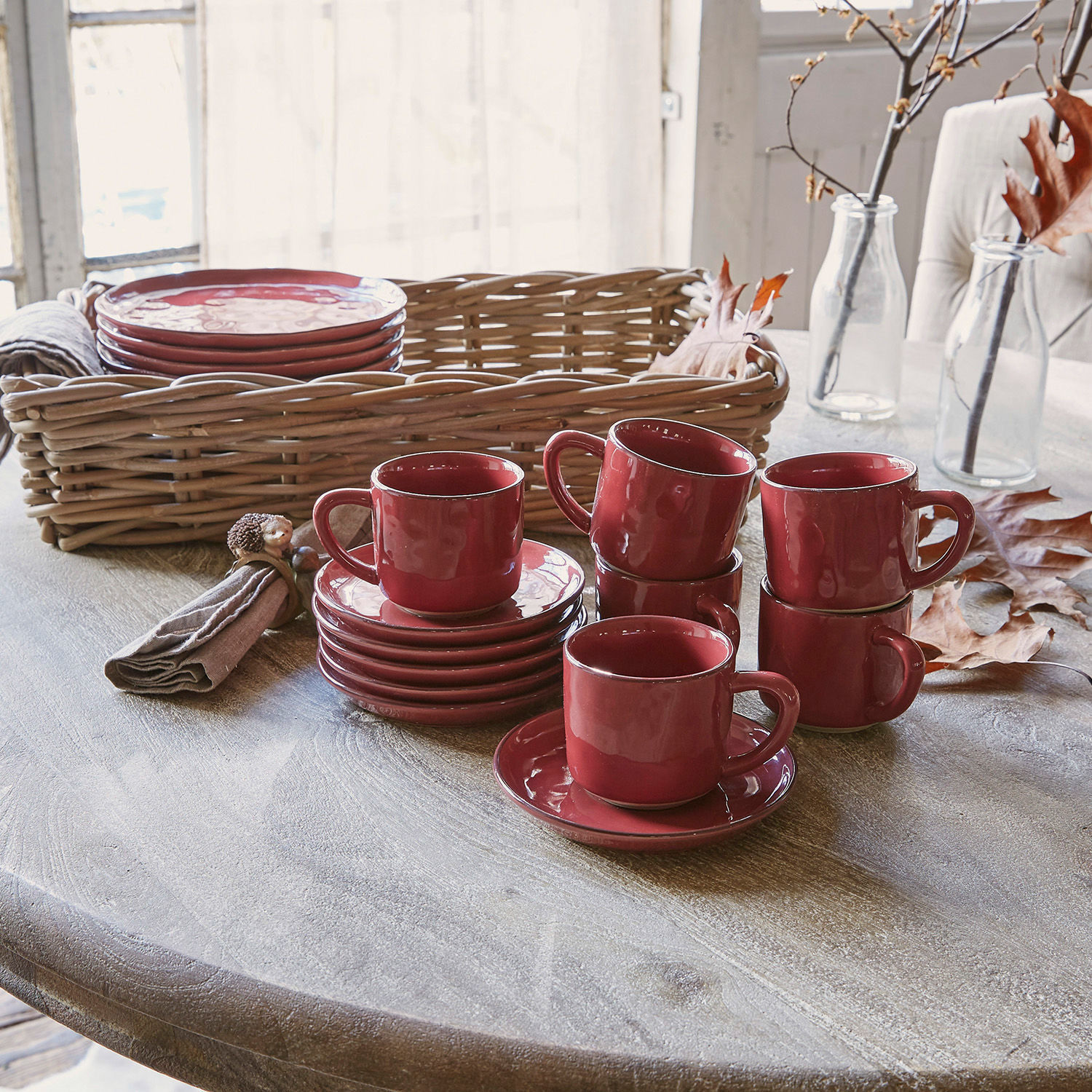 Tasse mit Untertasse 6er Set Biarré Set aus roten Keramiktassen und Untertassen auf Holztisch mit Weidenkorb im Hintergrund