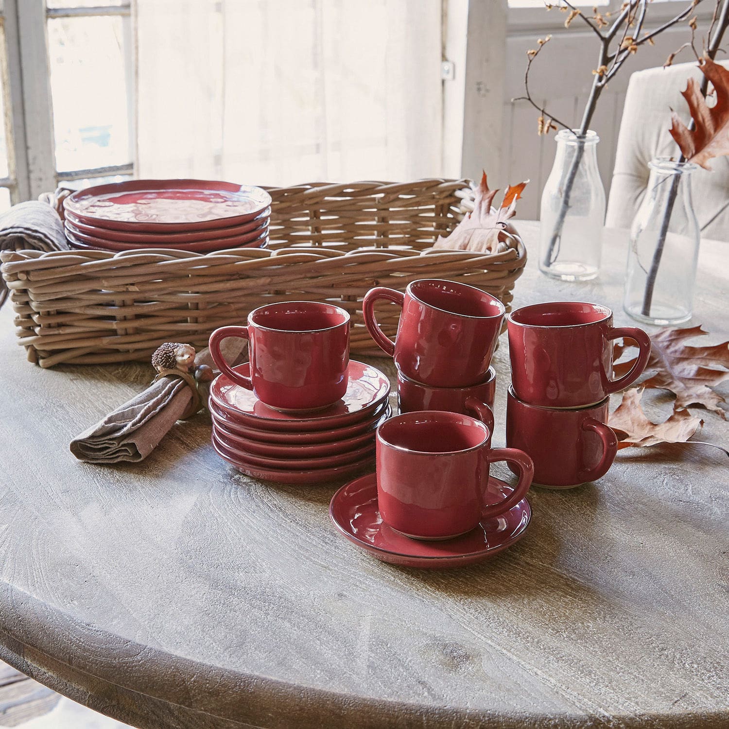 Tasse mit Untertasse 6er Set Biarré Set aus roten Keramiktassen und Untertassen auf Holztisch mit Weidenkorb im Hintergrund