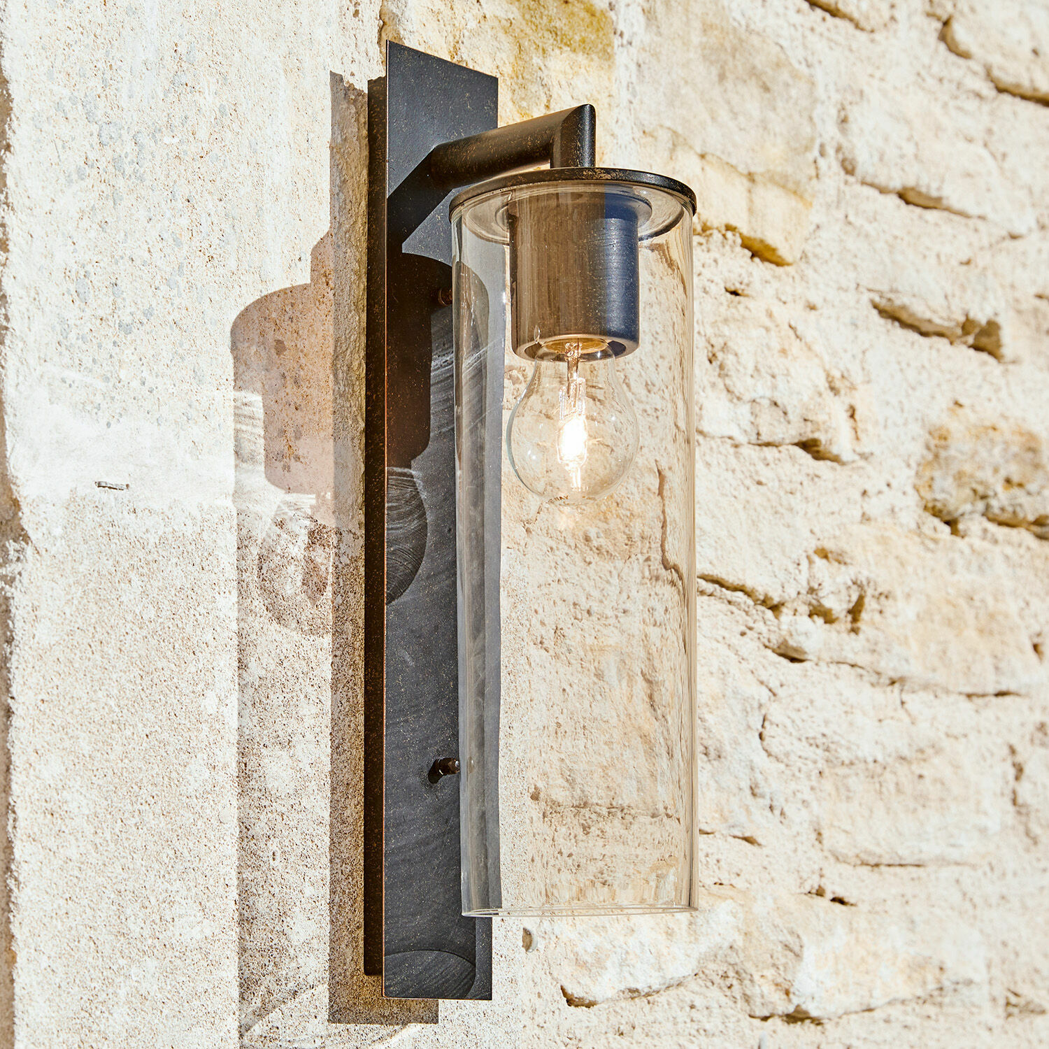 Außenwandlampe Clisson Schwarze Metall-Wandleuchte mit klarem Glaszylinder an heller Steinwand für Außenbereich