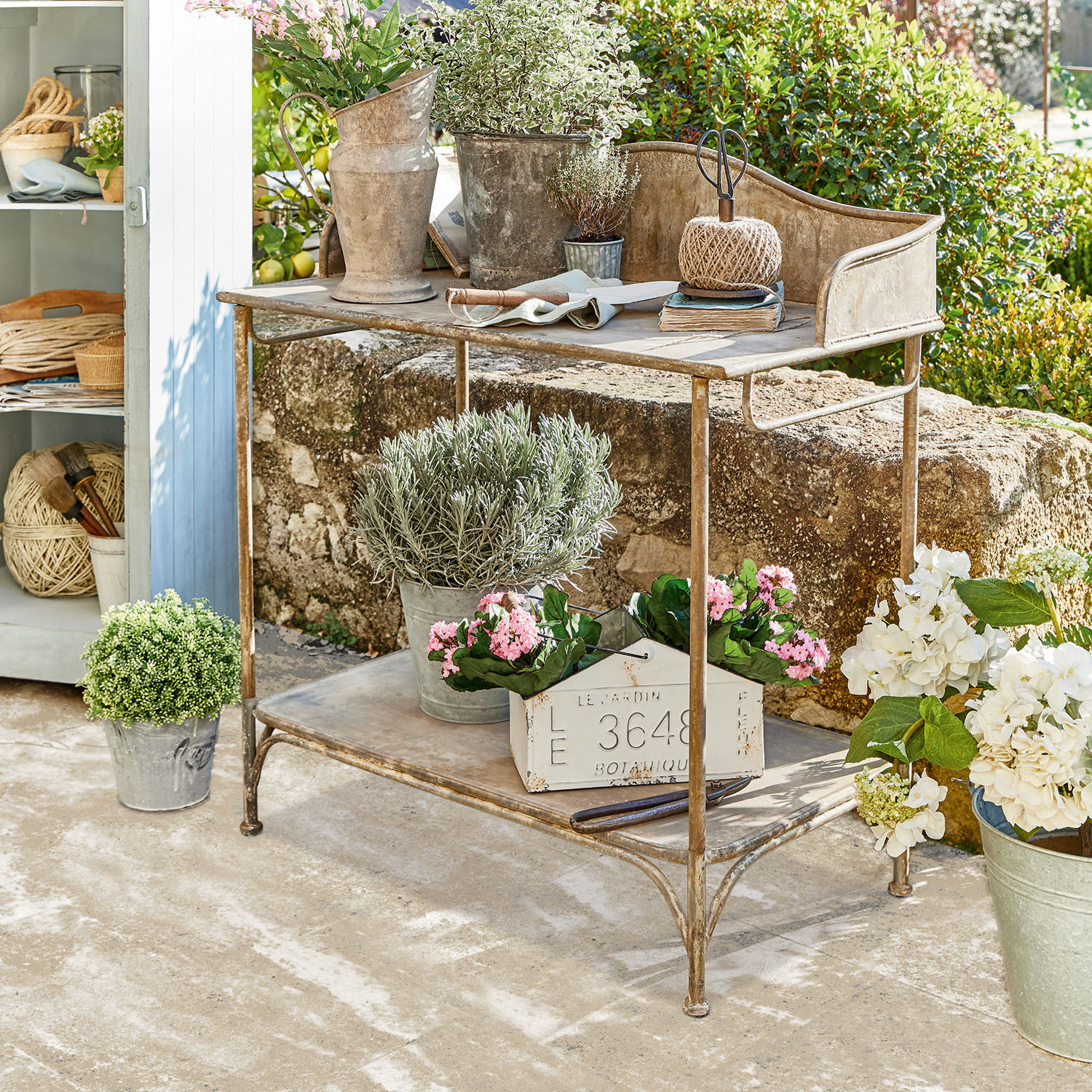 Pflanztisch Banners Metall-Gartentisch mit Pflanzen und Gartengeräten auf sonniger Terrasse dekoriert