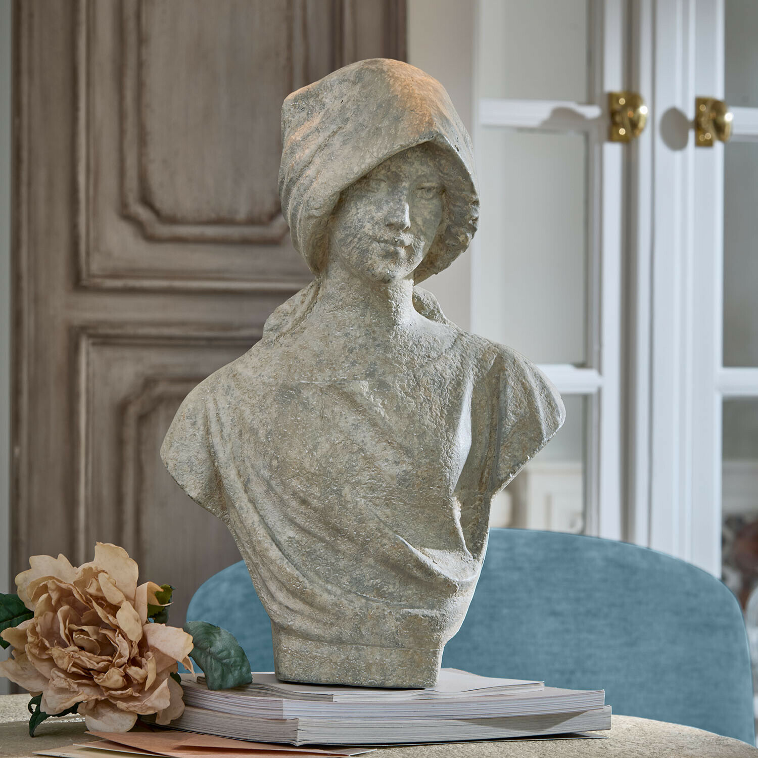 Graue Steinstatue einer Frau als Büste auf einem Bücherstapel mit dekorativer Blume daneben