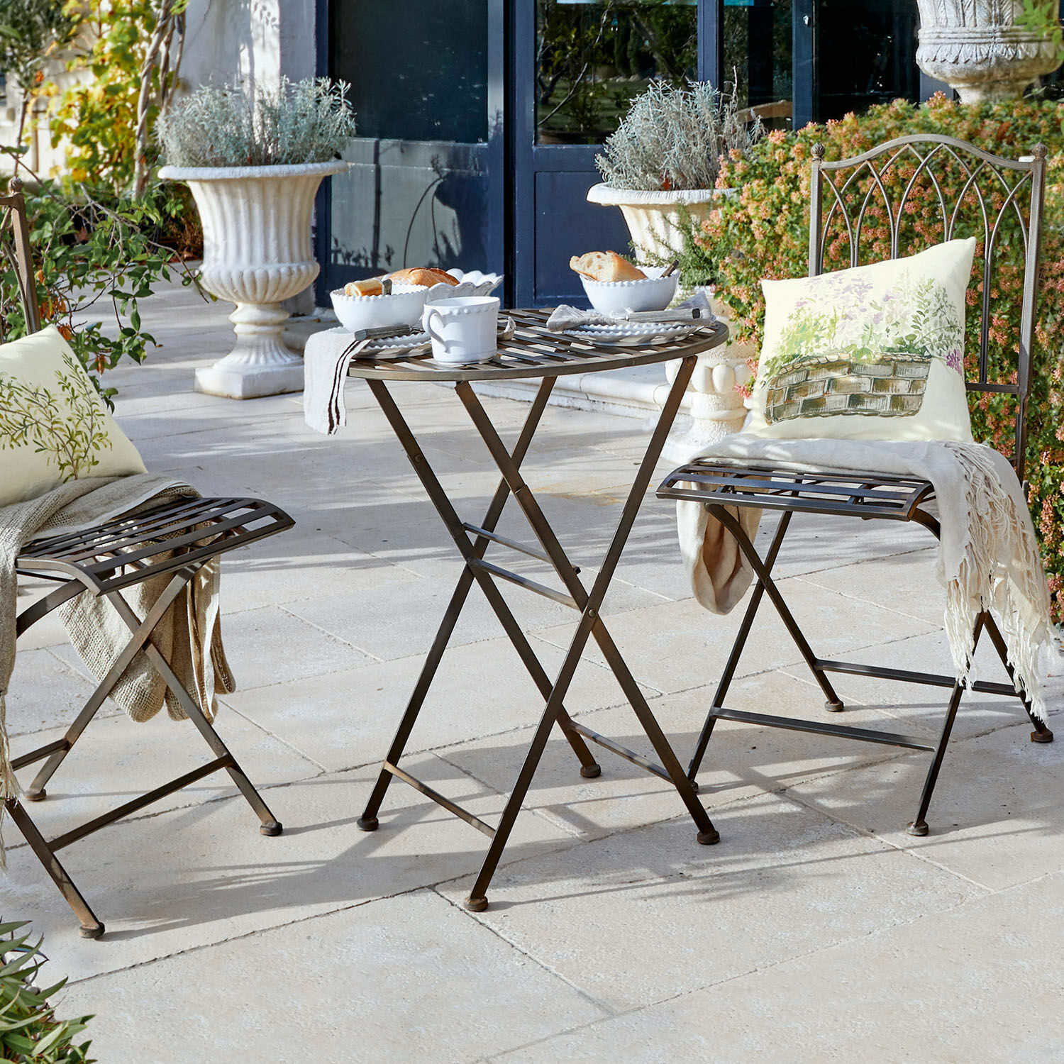 Tisch Brignoles Brauner Metall-Klapptisch und Stühle auf Terrasse mit dekorativen Kissen und weißem Geschirr