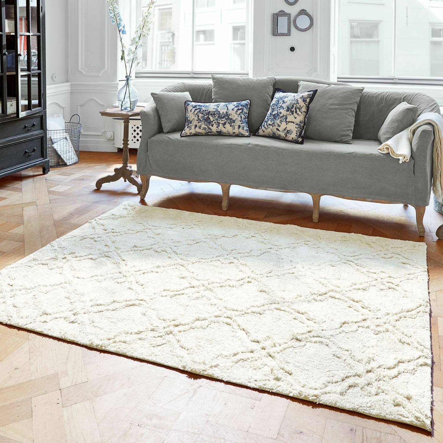 Teppich Petrus Heller cremefarbener Teppich mit weichem Muster auf Holzboden im Wohnzimmer mit grauem Sofa