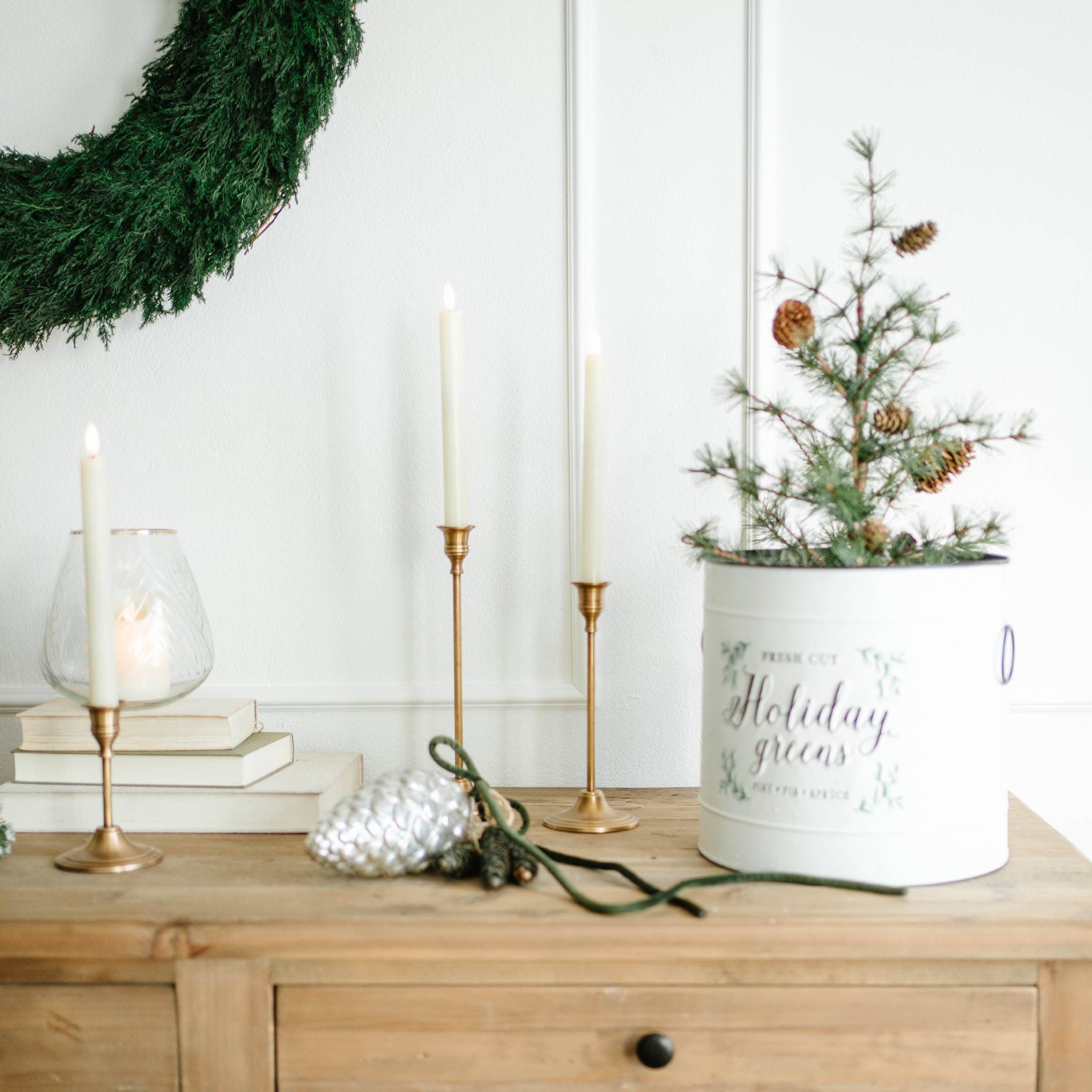 Weihnachtsdekoration mit grünem Kranz, goldenen Kerzenhaltern und weißem Behälter mit Zweigen und Zapfen