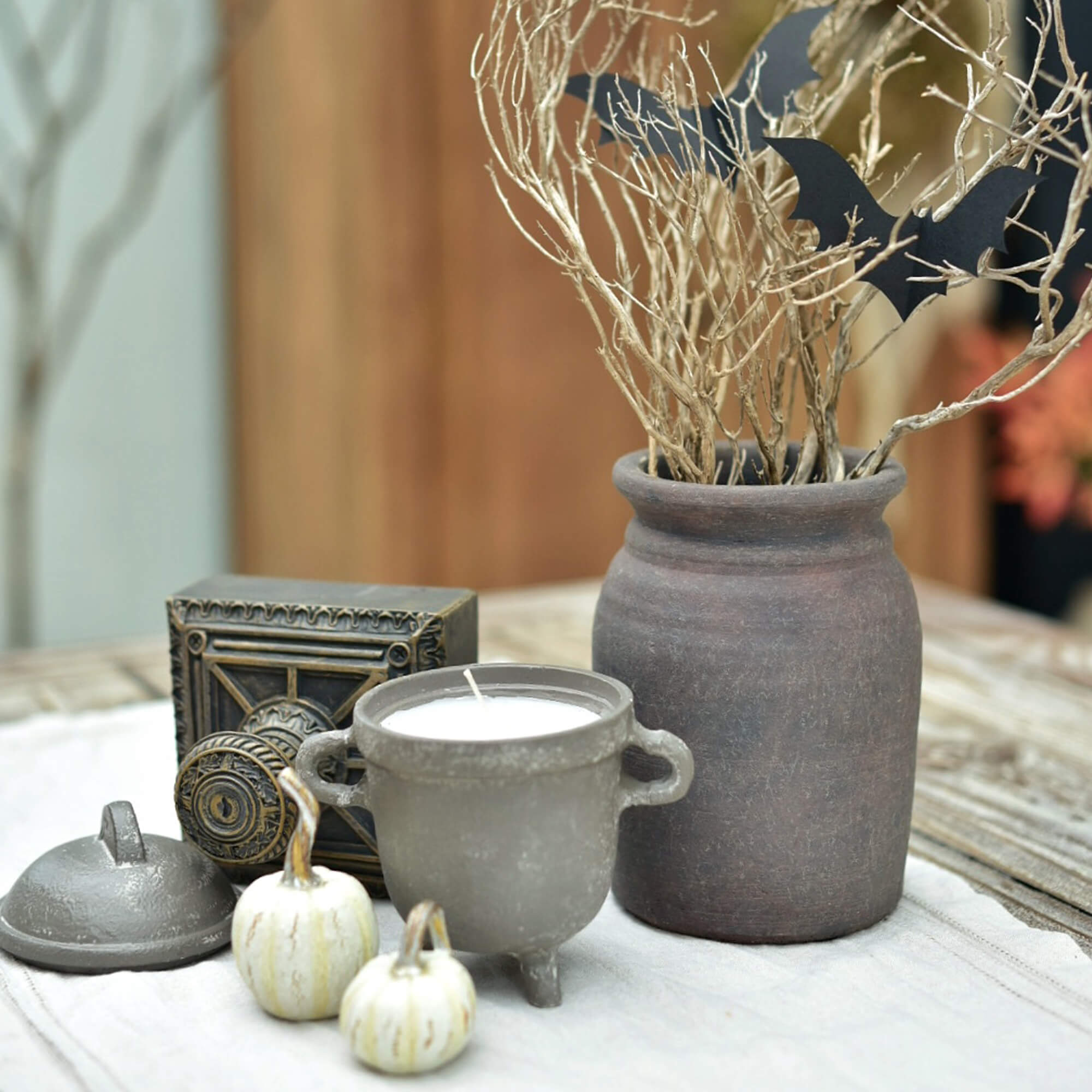Dekoratives Set mit Keramikkerze, Tonvase und weißen Mini-Kürbissen auf Tisch