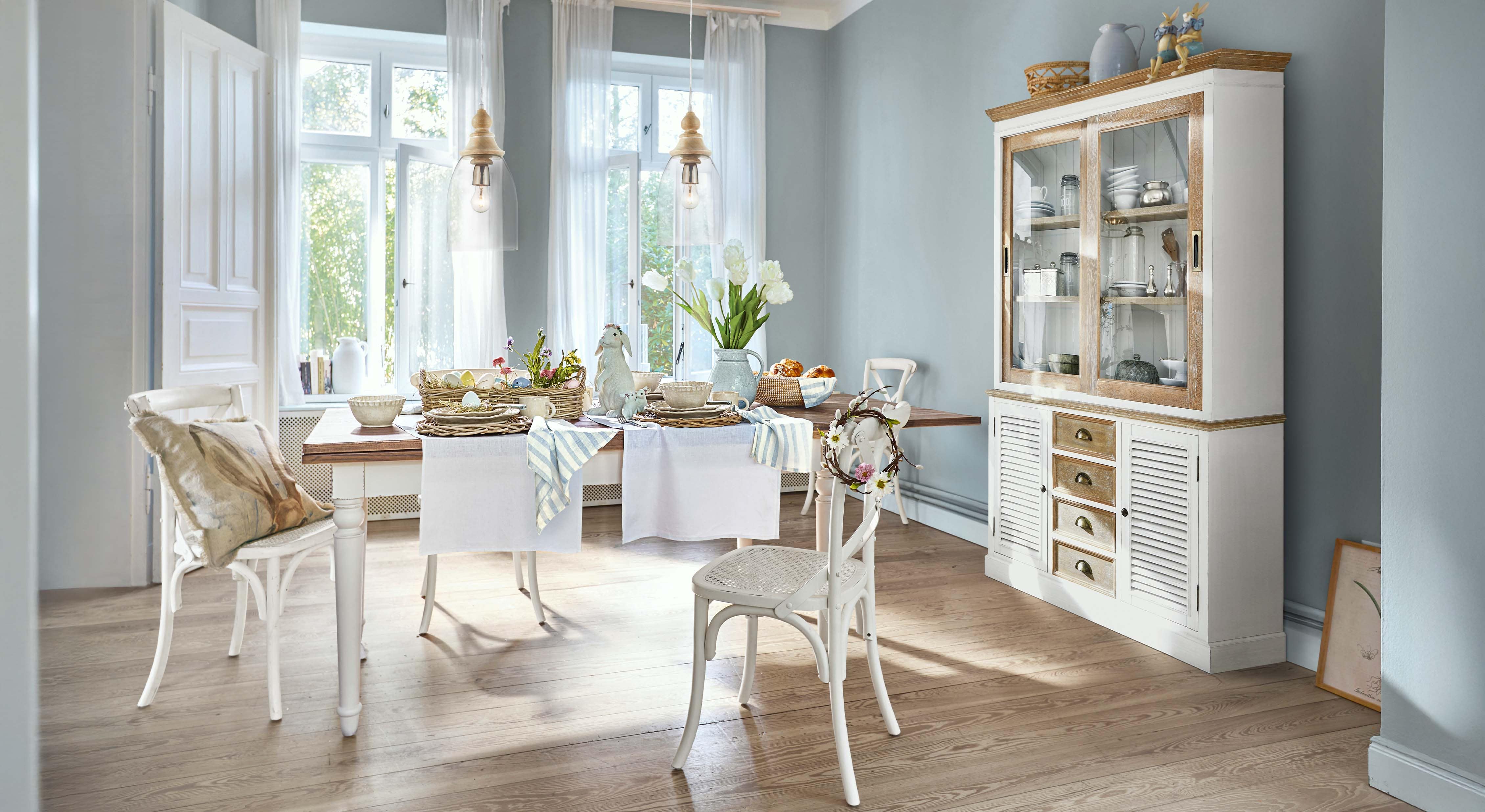 Esszimmer mit weißem Holztisch und Stühlen, Osterdekorationen und Vitrine mit Glastüren aus hellem Holz