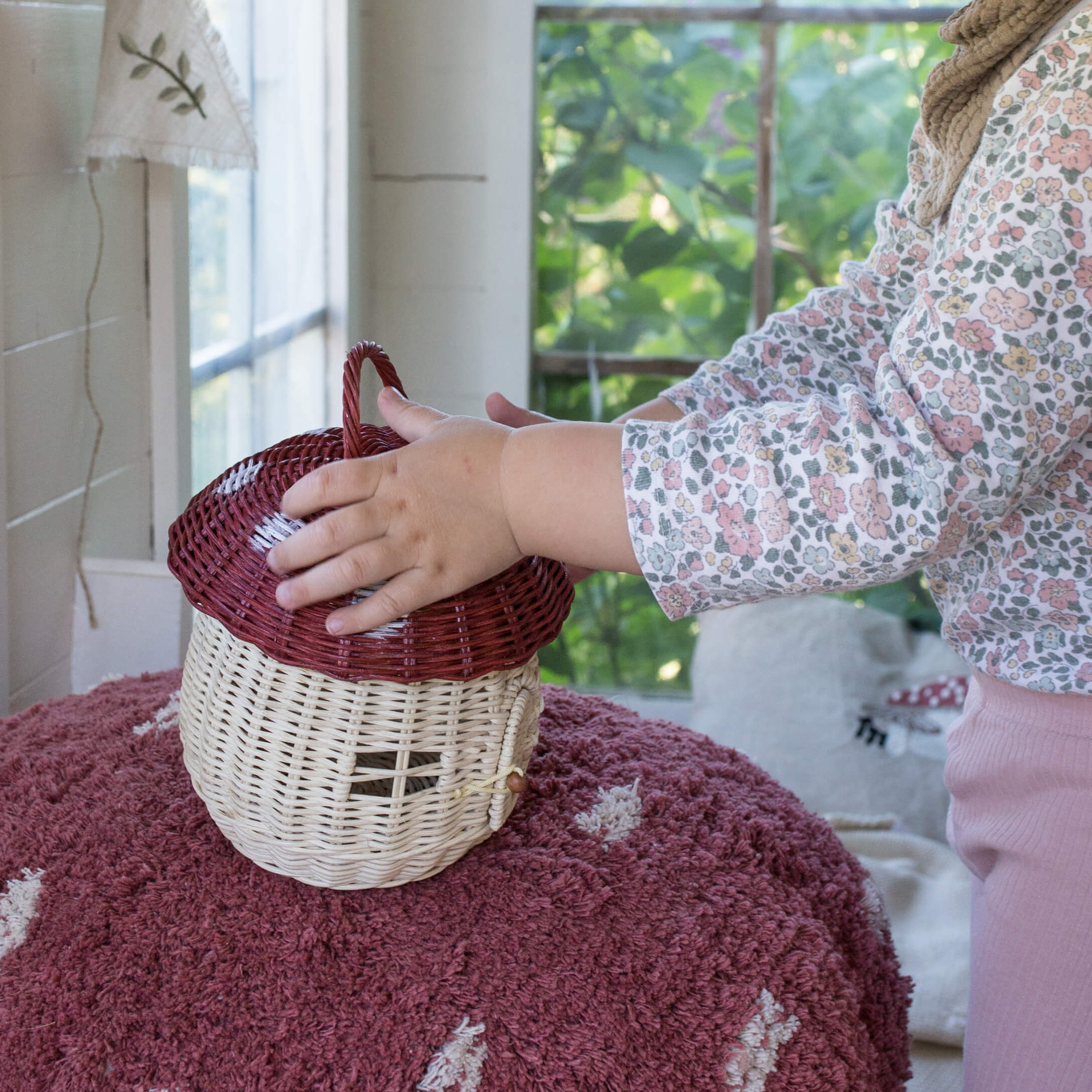Kind berührt naturfarbenen, pilzförmigen Korb aus Weide auf rosa Teppich im Zimmer