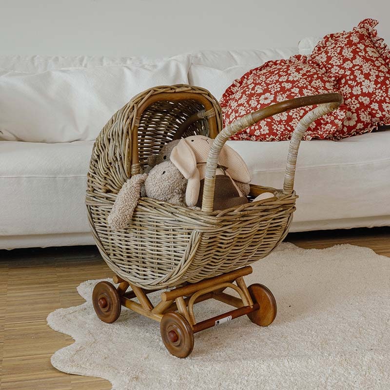 Kinderwagen aus Weide mit Holzrädern und Plüschtieren vor weißem Sofa in hellem Raum