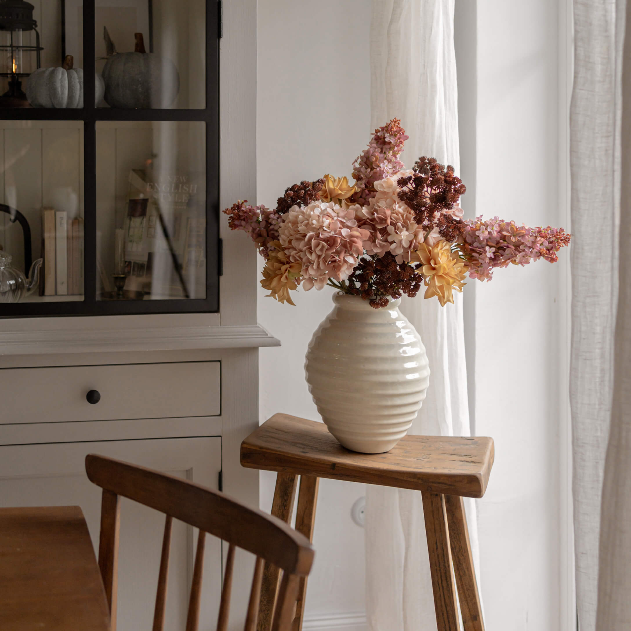 Weißer Alabastervase mit gelb-rosa Blumen auf Holzschemel in hellem Raum
