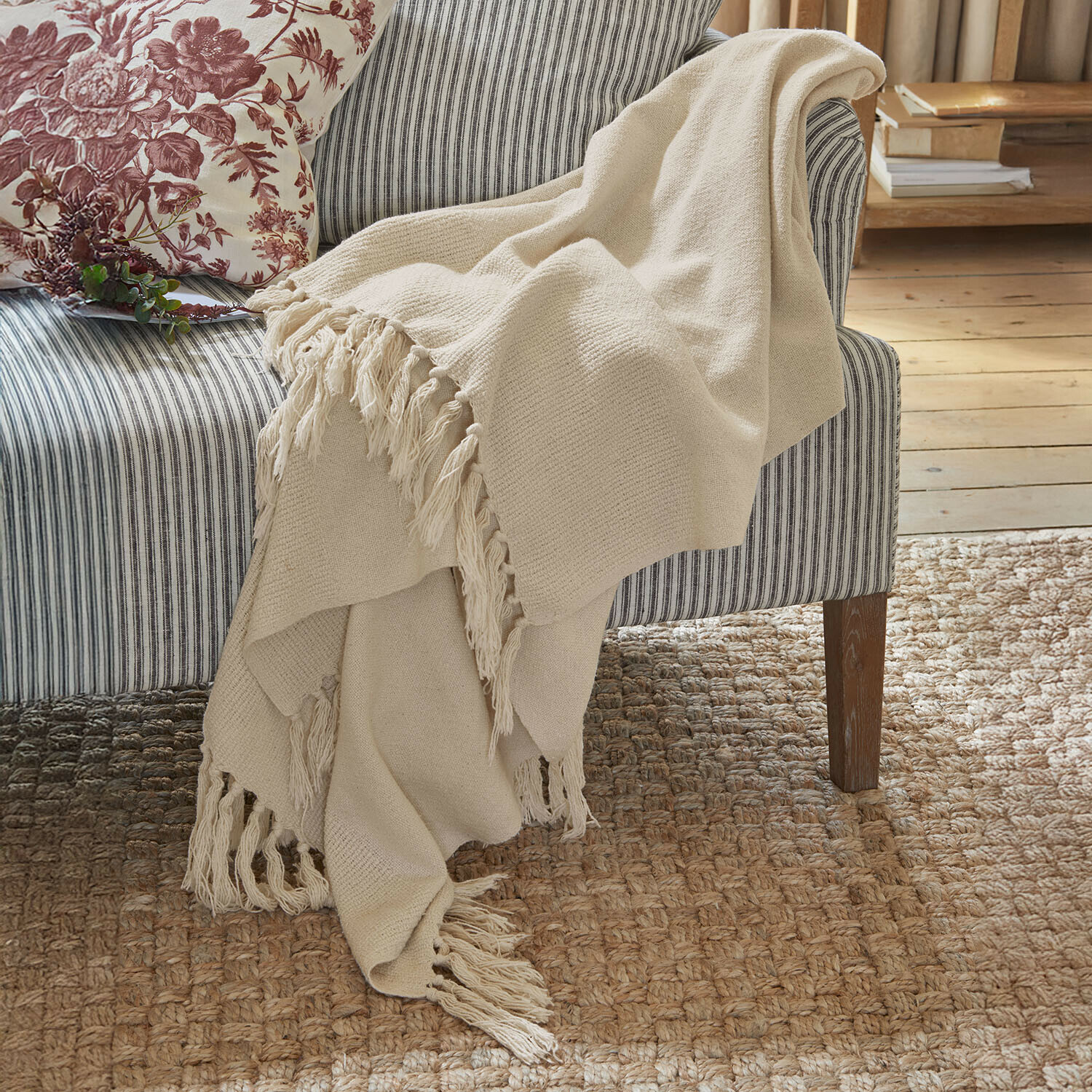 Plaid Skandira Beige Kuscheldecke mit Fransen aus weichem Stoff auf grauem, gestreiftem Sofa im gemütlichen Raum