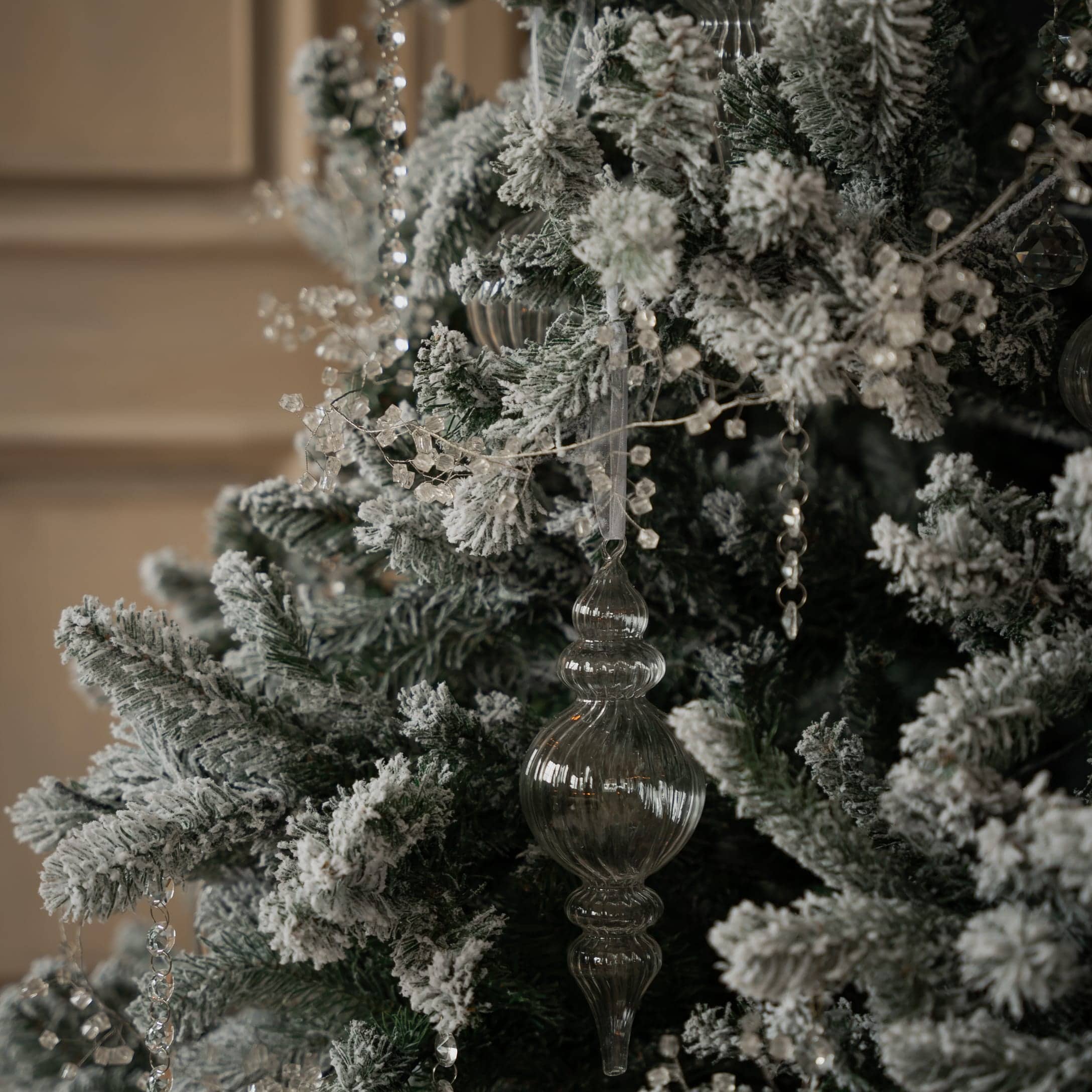Künstlicher Weihnachtsbaum mit weißem Schnee und transparenten Glasornamenten