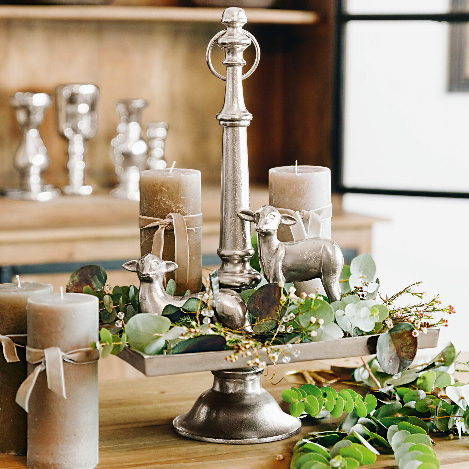 Stylebox Osterlamm Osterlamm Silberne Metall-Etagere mit Kerzen, grünen Blättern und dekorativen Schaf-Figuren als Tischdeko
