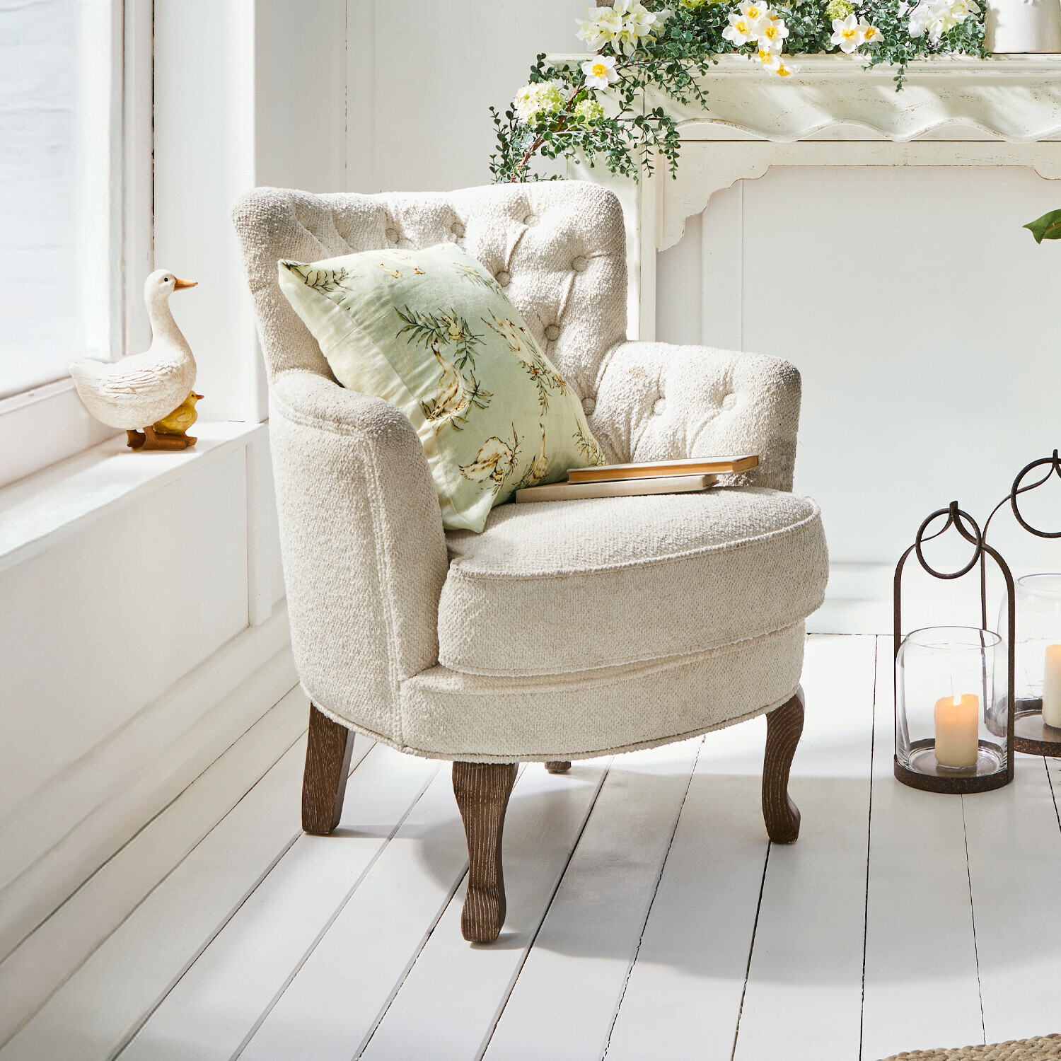 Beiger Sessel aus weichem Stoff mit Holzbeinen und grünem Blumenmuster-Kissen in hellem Raum