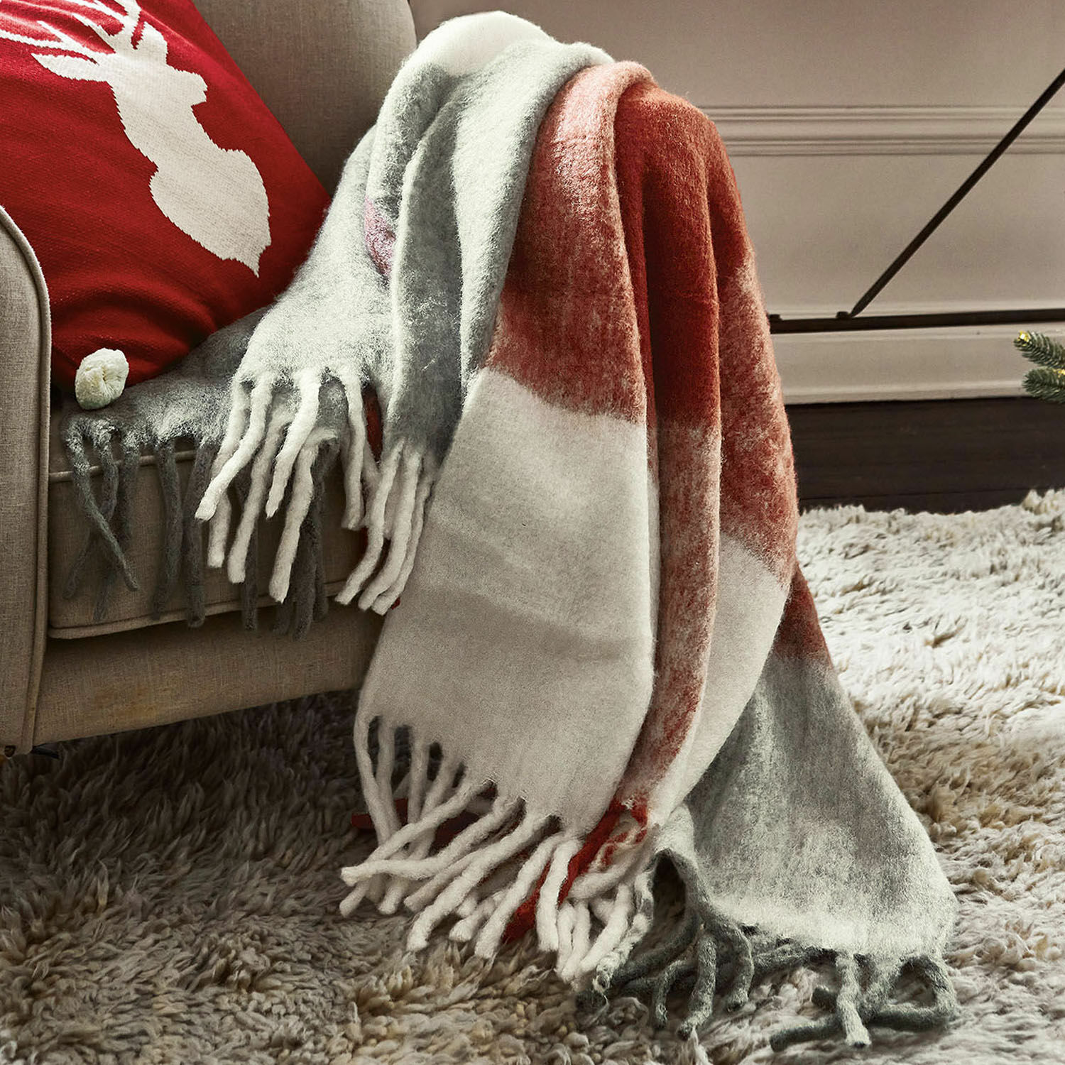 Plaid McGreg Weiche Kuscheldecke mit Fransen in Grau, Weiß und Rot auf beigem Sofa, gemütliche Wohnraumdeko