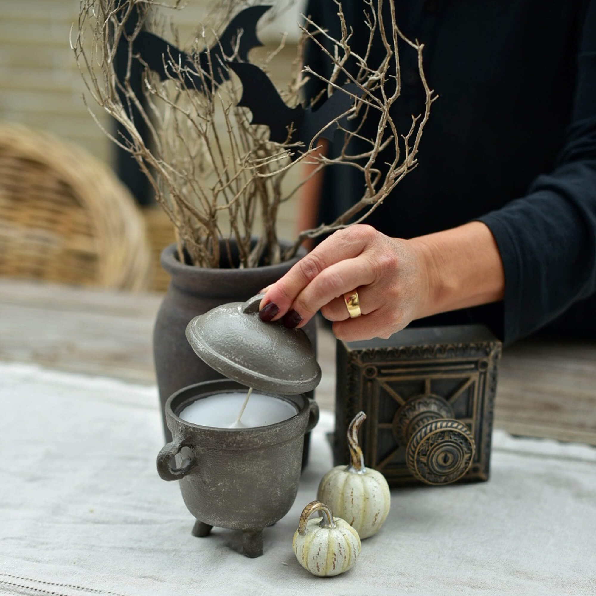 Graue Kerze in Kesselform mit Deckel auf Halloween-Tisch mit Kürbis- und Zweigdekorationen