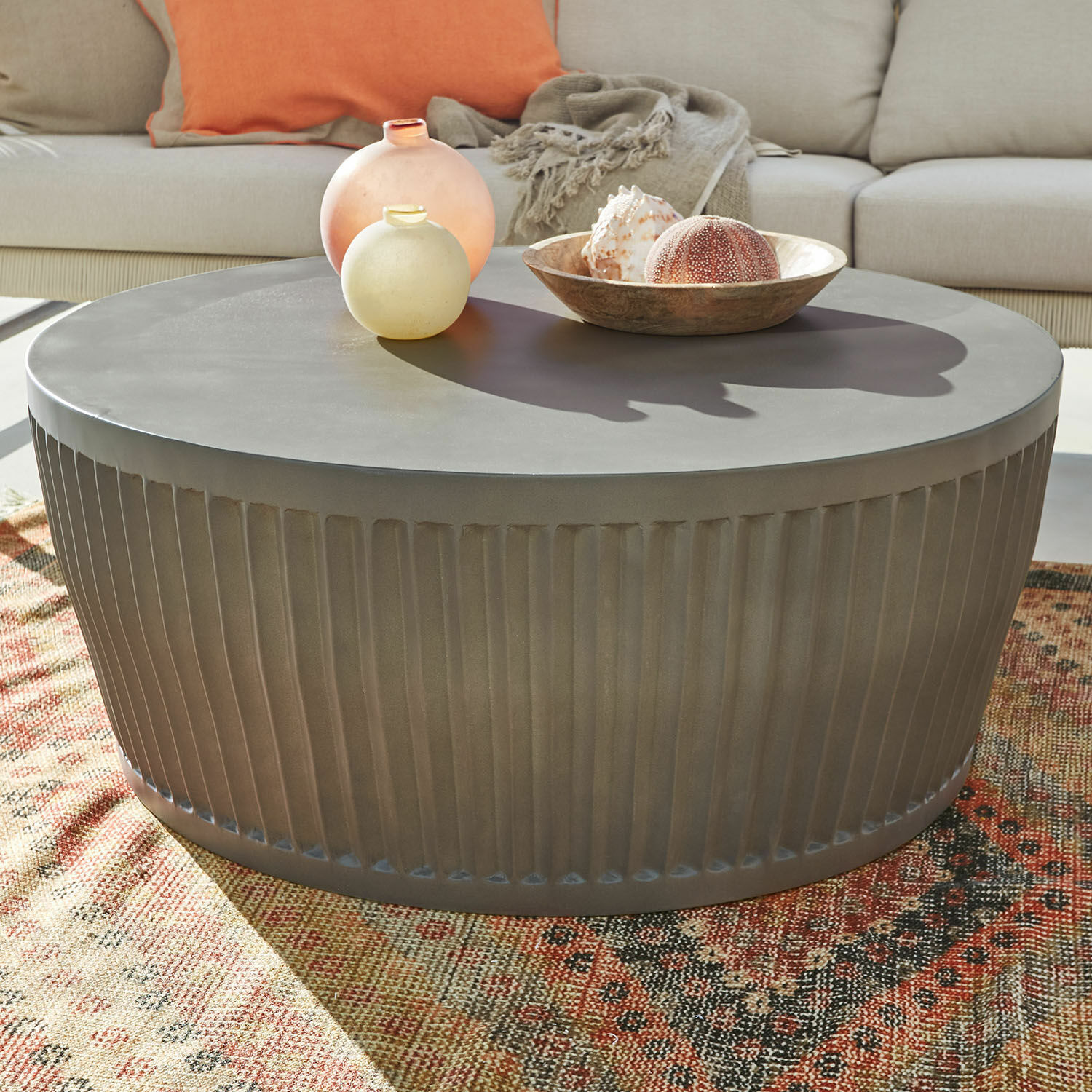 Couchtisch Vesalune Runder Couchtisch aus grauem Metall mit geriffeltem Sockel auf buntem Teppich im Wohnzimmer