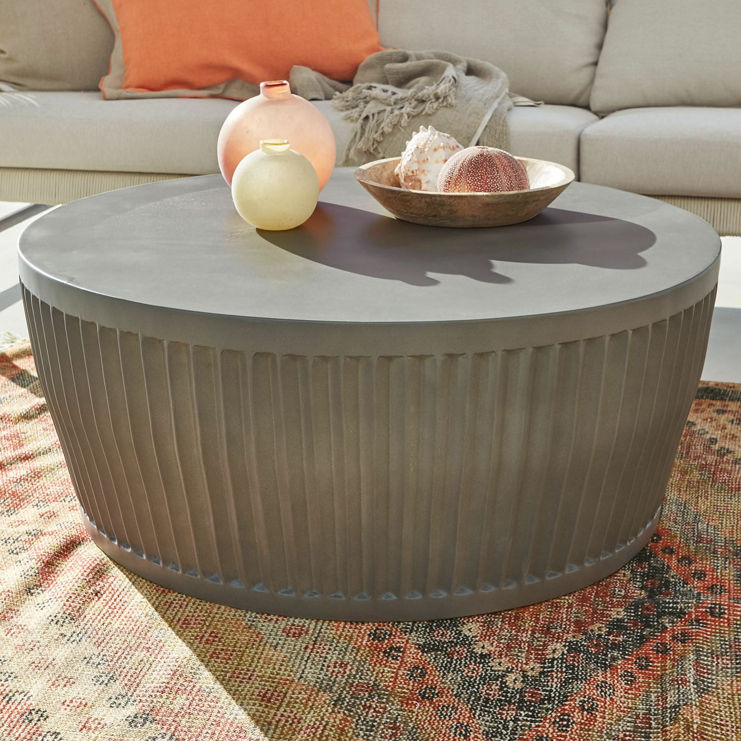 Couchtisch Vesalune Runder Couchtisch aus grauem Metall mit geriffeltem Sockel auf buntem Teppich im Wohnzimmer