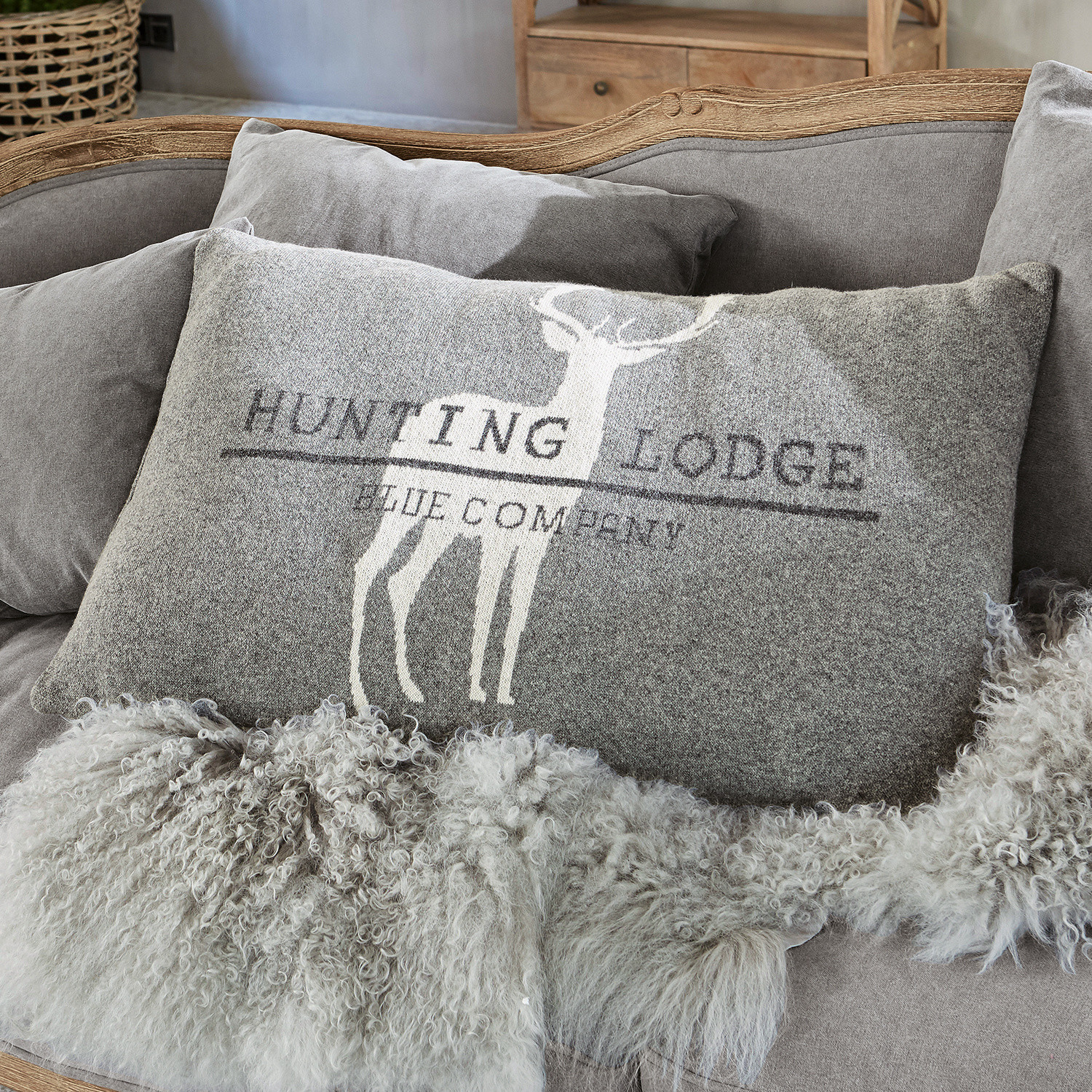 Kissen Lodge Graues Dekokissen mit Hirschmotiv und Schriftzug auf weichem Sofa mit Fellüberwurf