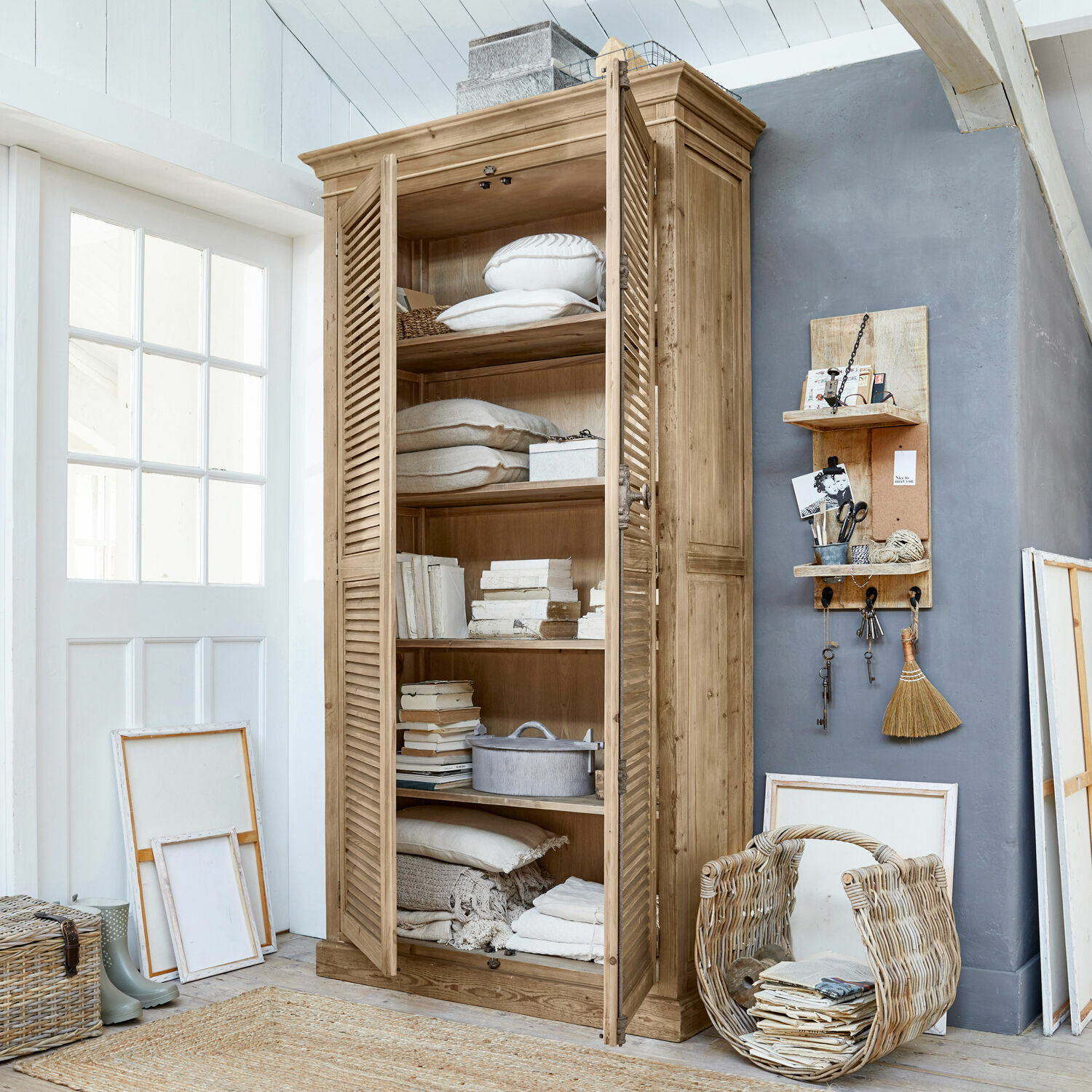 Schrank Farnham Holzschrank mit Lamellentüren in Naturholzfarbe, gefüllt mit Kissen und Büchern in hellem Raum