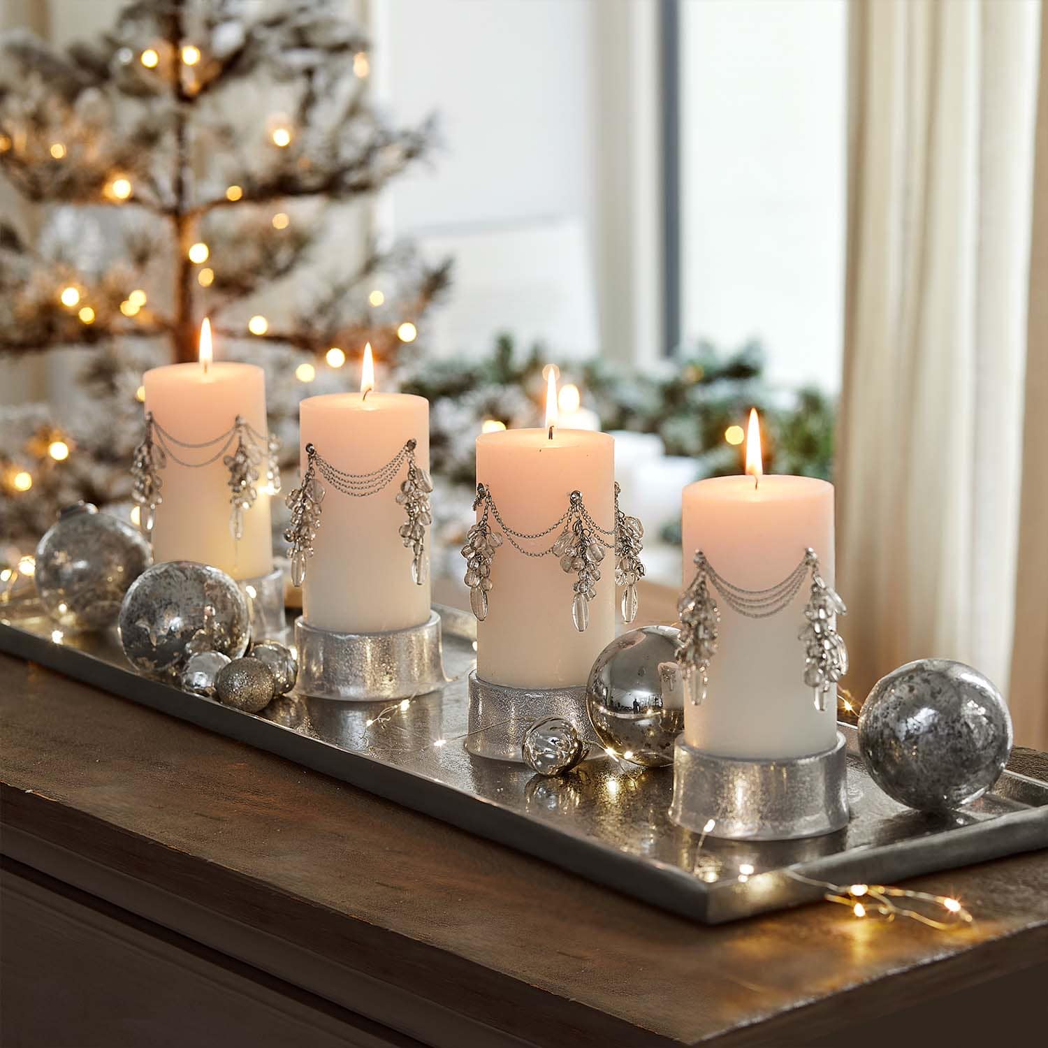 Vier weiße Kerzen mit silbernen Ketten und Kristallanhängern auf silbernem Tablett mit Weihnachtsdeko
