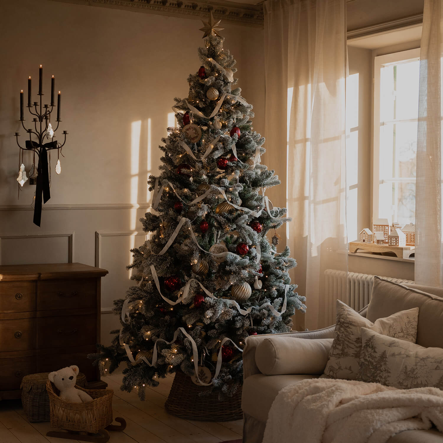 Gemütliches Wohnzimmer mit schneebedecktem Weihnachtsbaum, roten und goldenen Kugeln und weißem Band