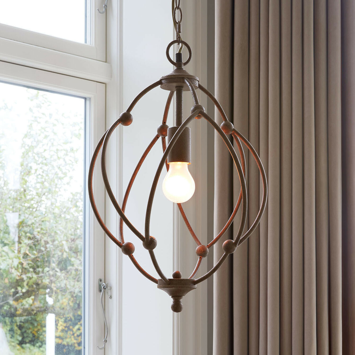 Hängelampe aus rostigem Metall mit kugelförmigem Gestell und sichtbarer Glühbirne für rustikales Ambiente.