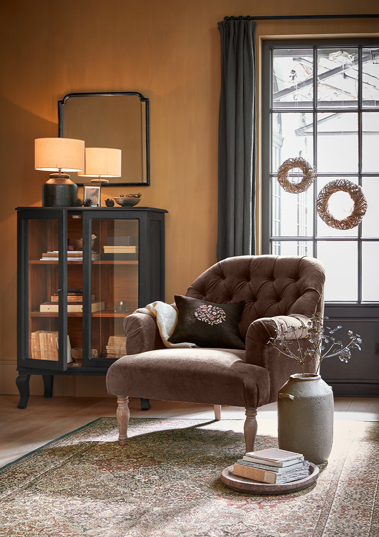 Brauner Polstersessel mit Kissen und grauem Schrank mit Lampe in gemütlichem Wohnzimmer mit Teppich