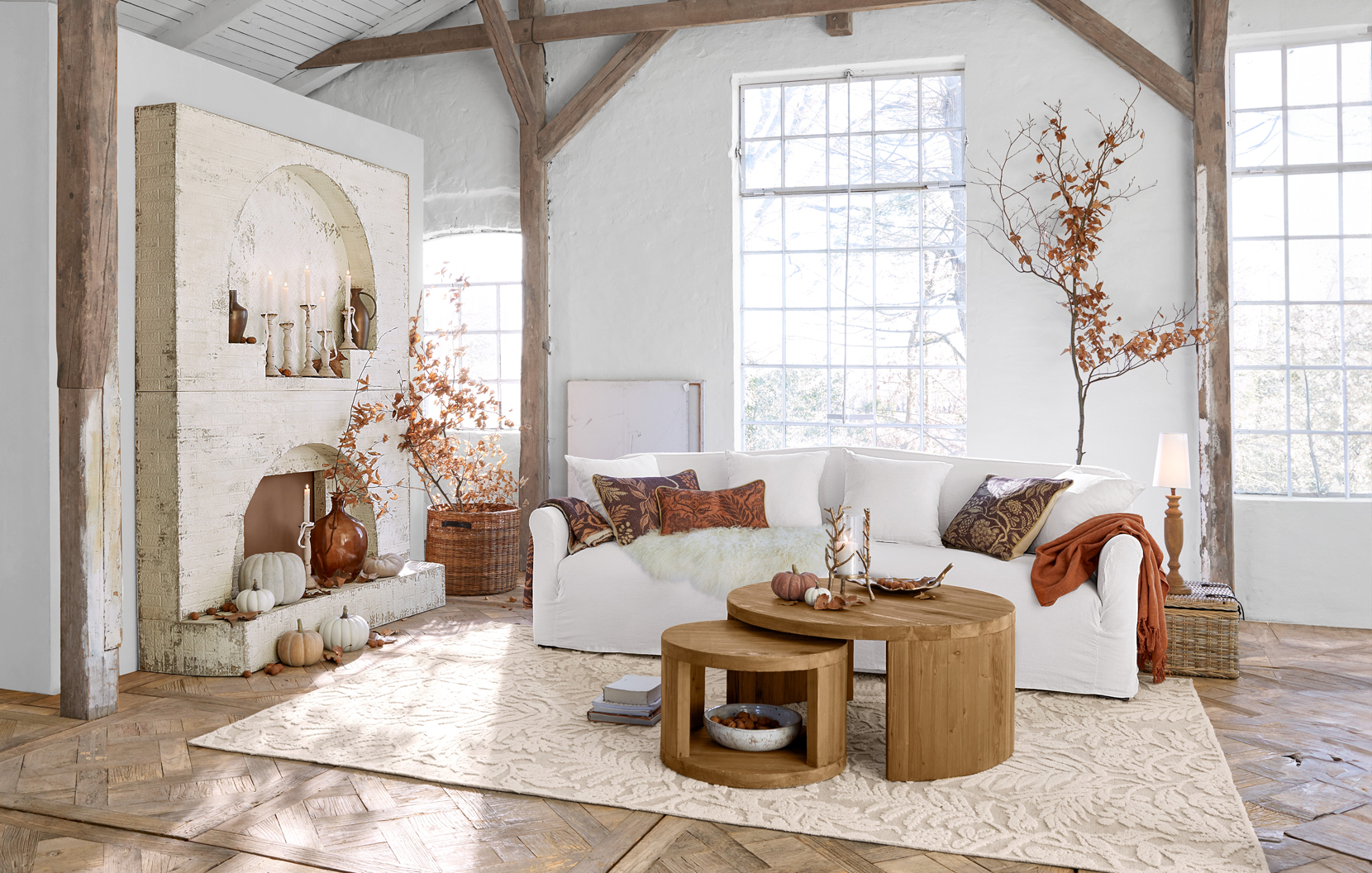 Gemütliches Landhaus-Wohnzimmer mit weißem Sofa, runden Holztischen und herbstlicher Dekoration in Braun- und Beigetönen