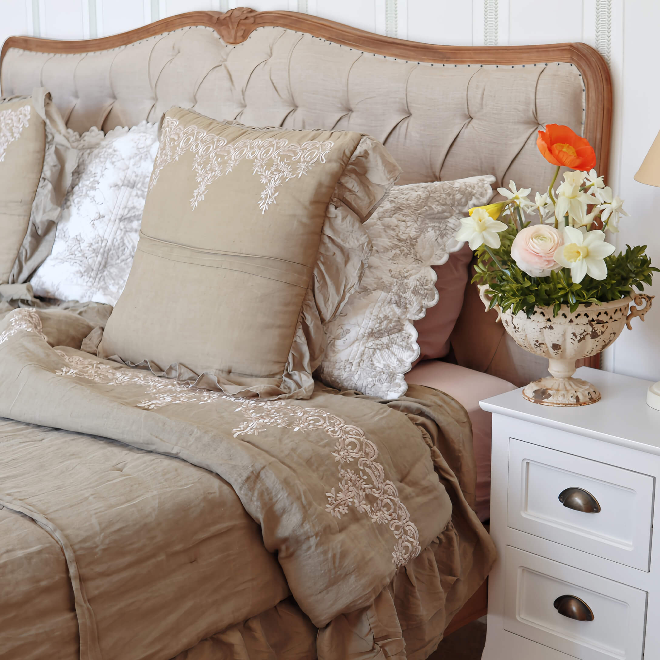 Beige Bettwäsche mit bestickten Kissen und Decke auf einem Bett mit gepolstertem Kopfteil