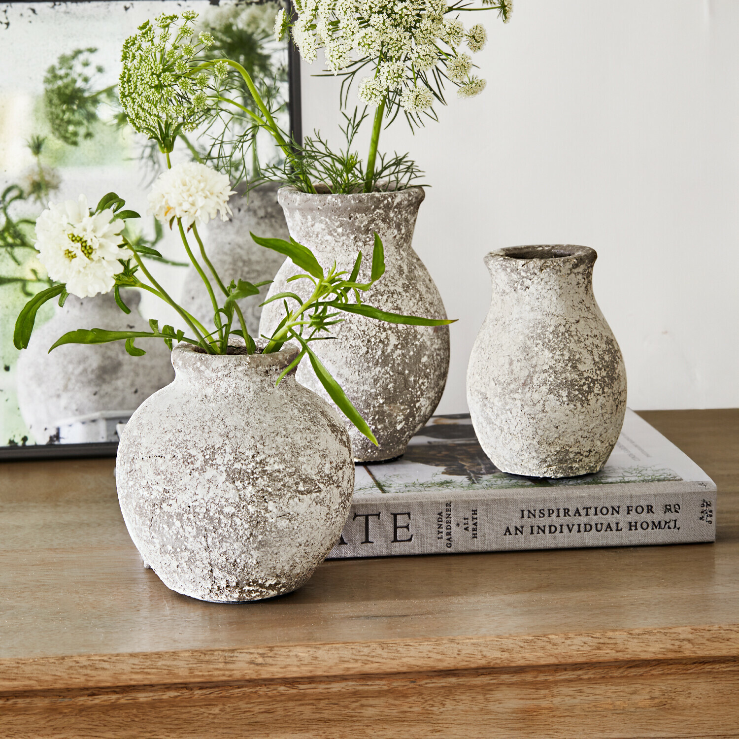 Drei rustikale Steinvase in Grau-Weiß auf Holztisch mit weißen Blumen dekoriert