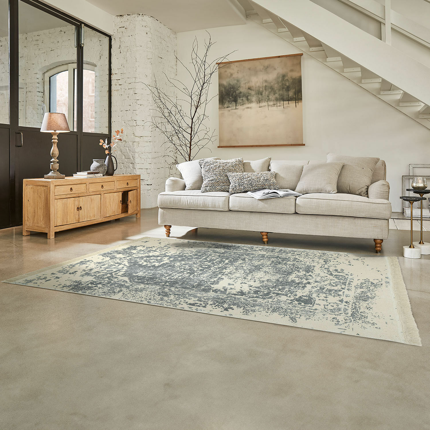 Beige Sofa mit Kissen auf grauem Teppich in hellem Wohnzimmer mit Holzkommode und Wanddekoration