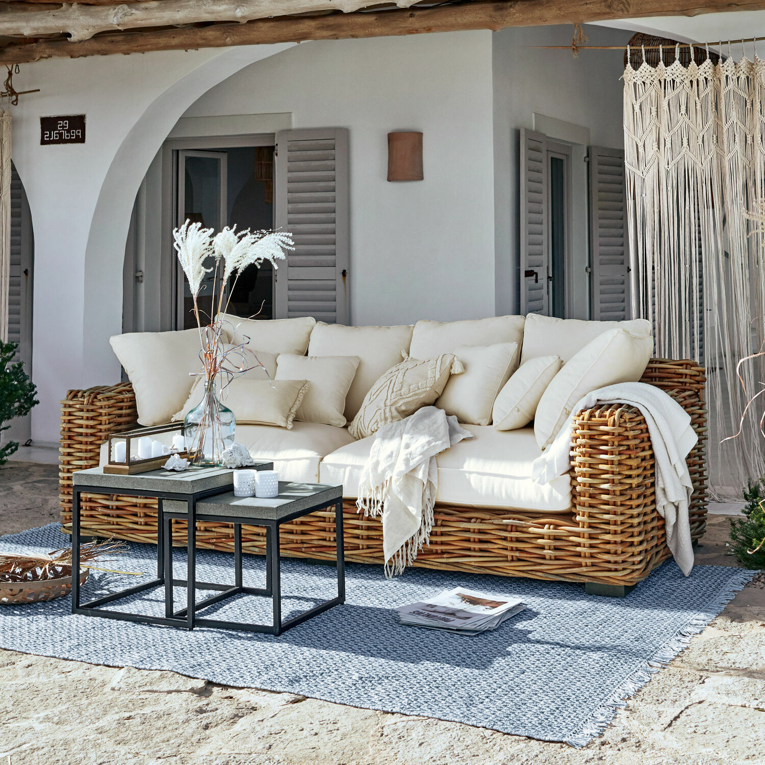 Sofa Rimini Rattansofa mit cremefarbenen Kissen und Decke auf blauem Teppich auf sonniger Terrasse
