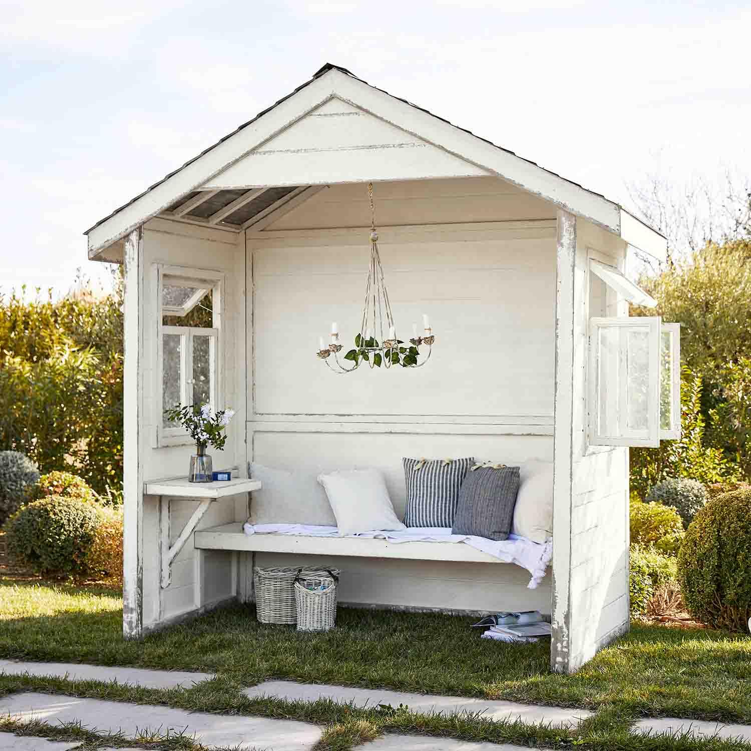 Weiße Holz-Gartenlaube mit Bank, Kissen und hängendem Kerzenleuchter, gemütlicher Rückzugsort
