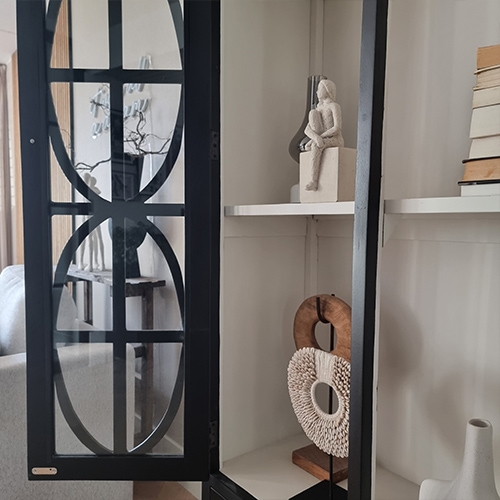Schwarze Metallvitrine mit dekorativen Regalen und Skulpturen in hellem Wohnzimmer
