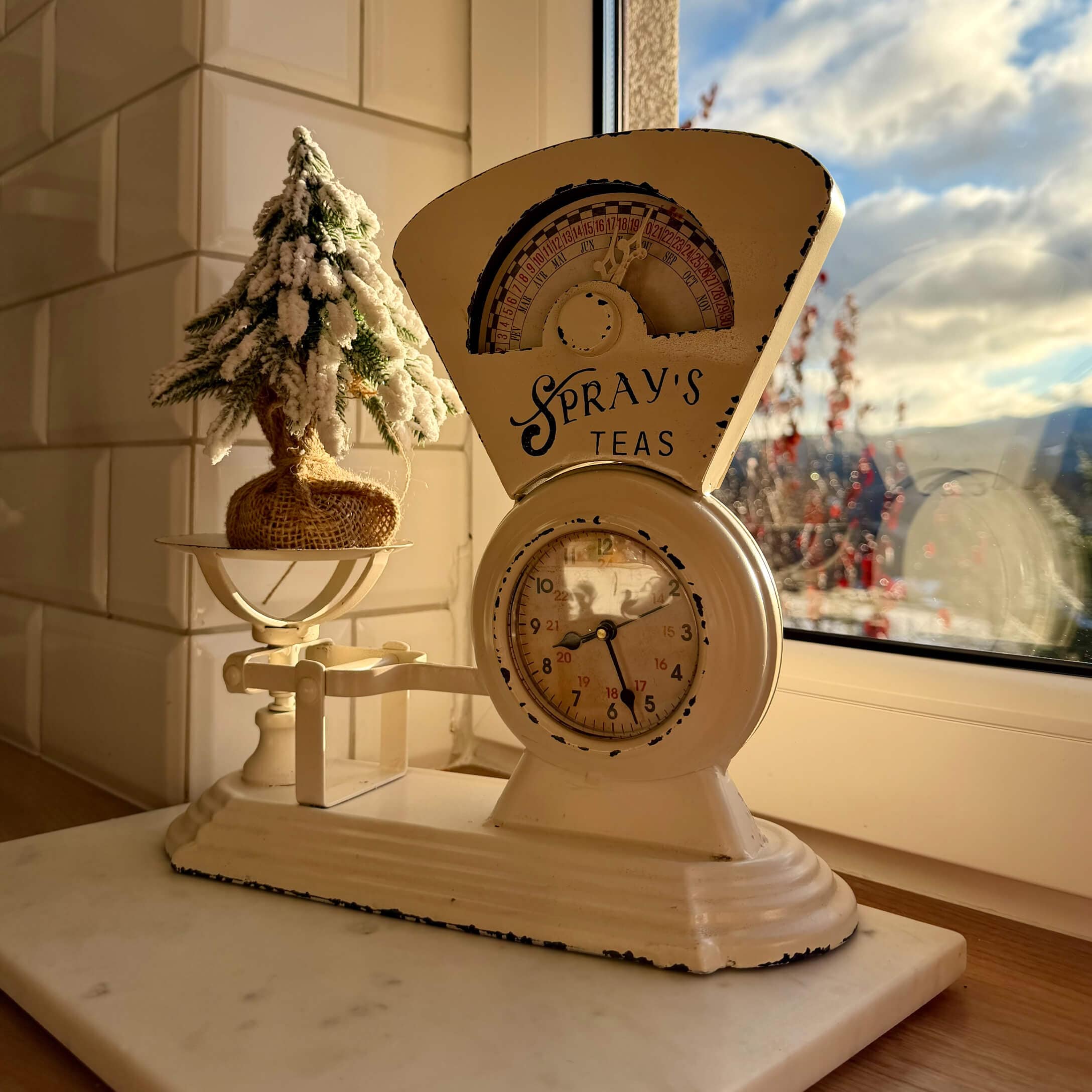 Beige Metall-Küchenwaage mit Uhr und Weihnachtsdeko auf Fensterbank im warmen Licht